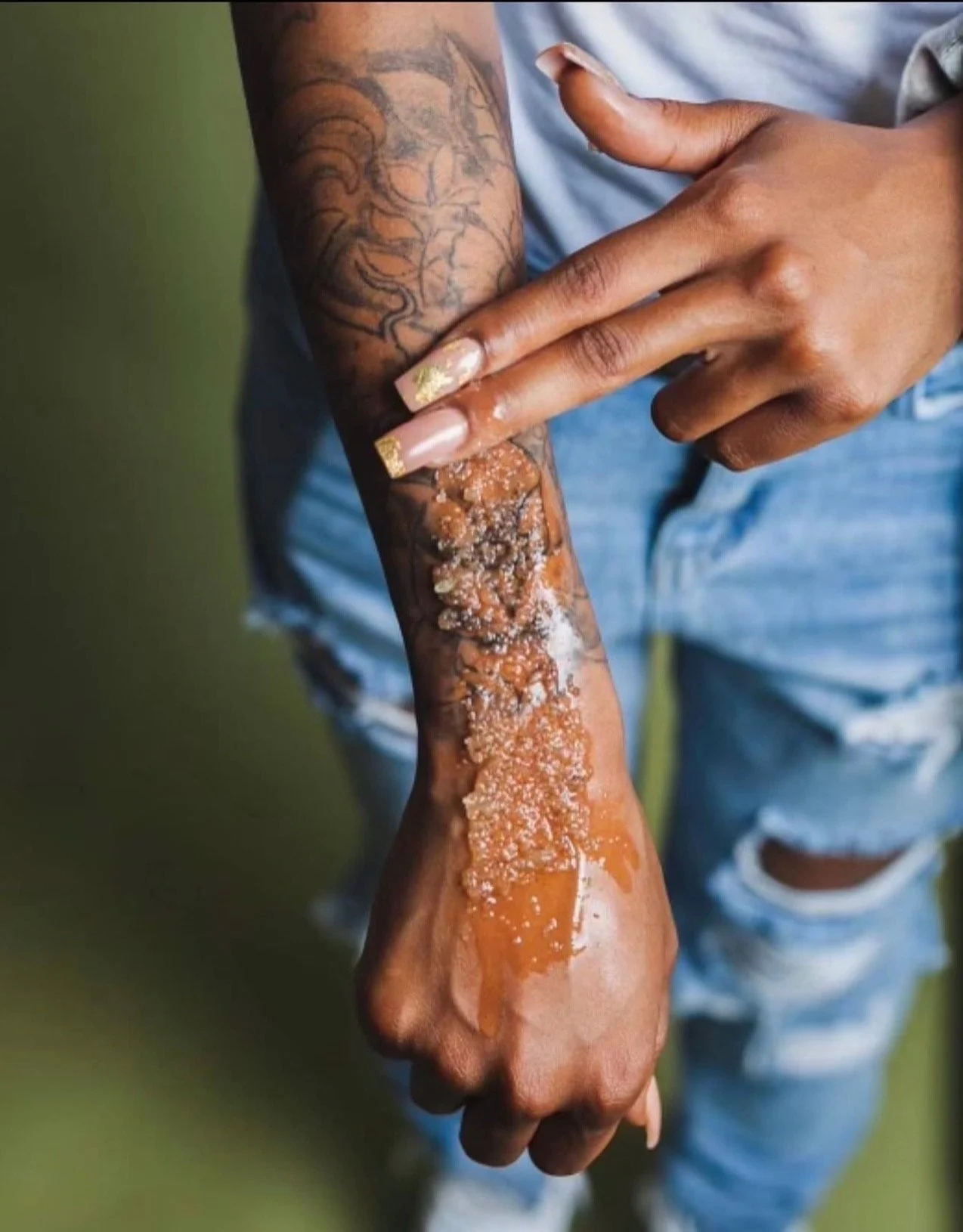 A person with tattoos on their arm is applying honey or syrup on their hand.