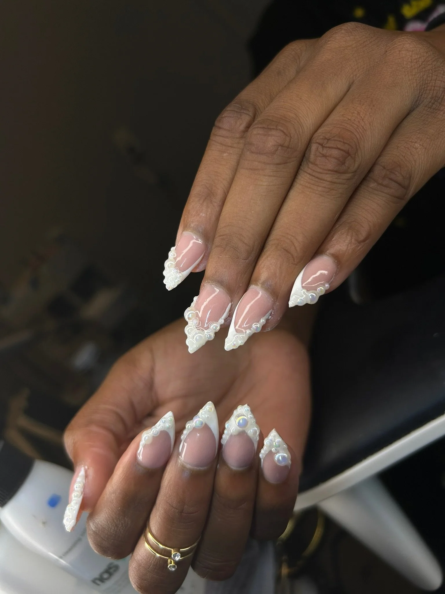 Close-up of two hands showing off elaborate white French manicure nails with 3D pearl and swirl designs.