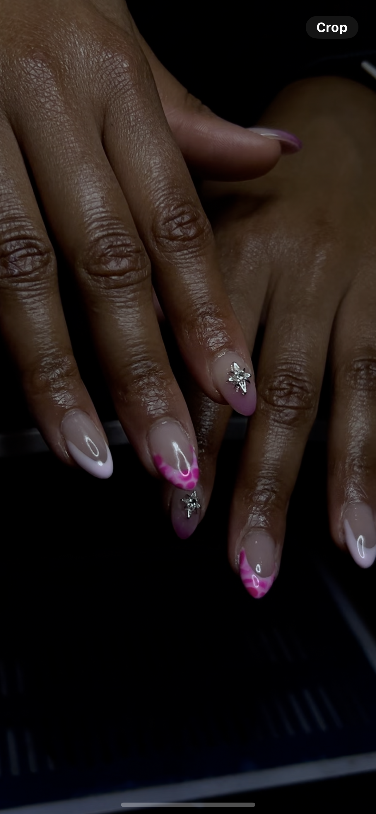 Close-up of hands with manicured nails featuring pink and white designs, and decorative silver star-shaped embellishments.