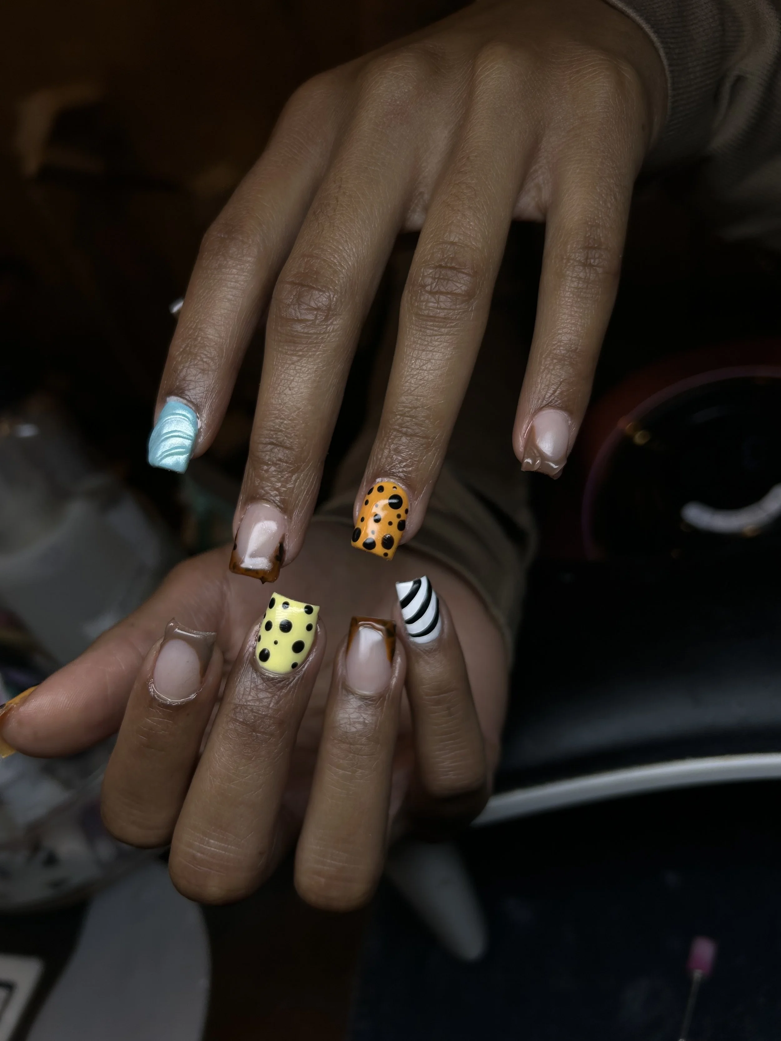 Close-up of a hand with colorful decorated nails featuring various patterns like stripes, polka dots, and waves.
