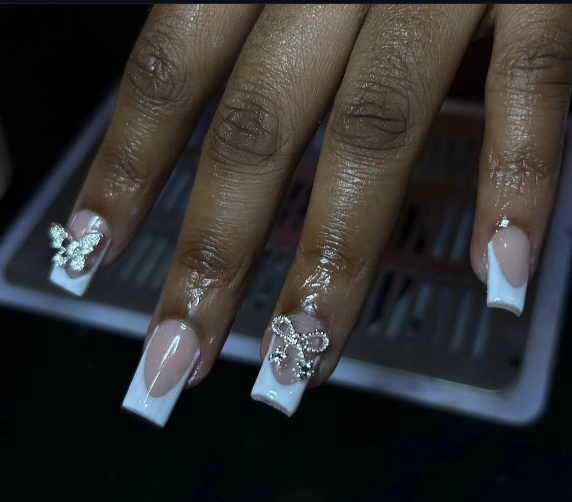 Close-up of a hand with long, decorated nails featuring white French tips and rhinestone embellishments.