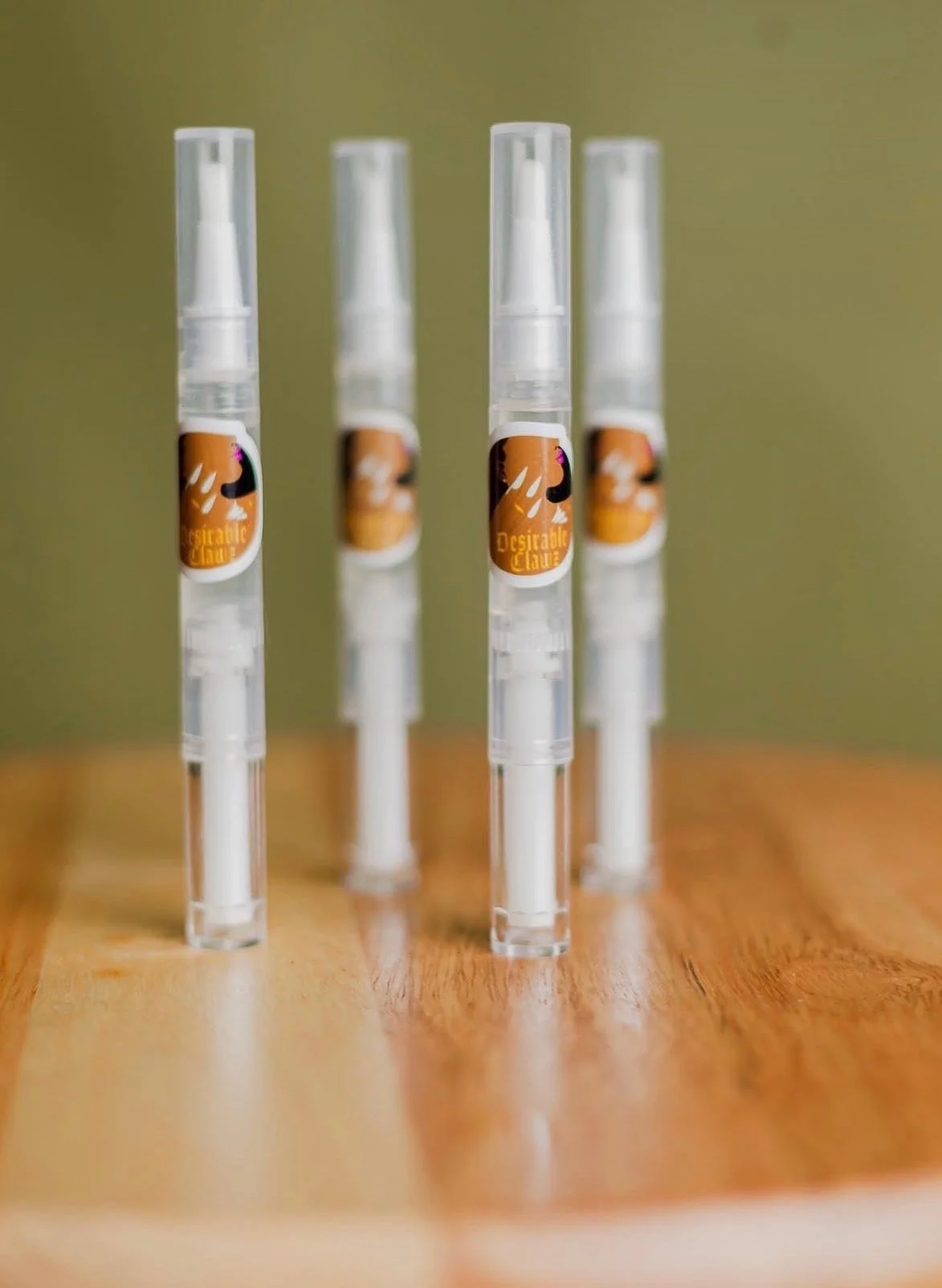 Four clear spray bottles with white labels featuring a black and orange design are positioned in a row on a wooden surface, with a green background.