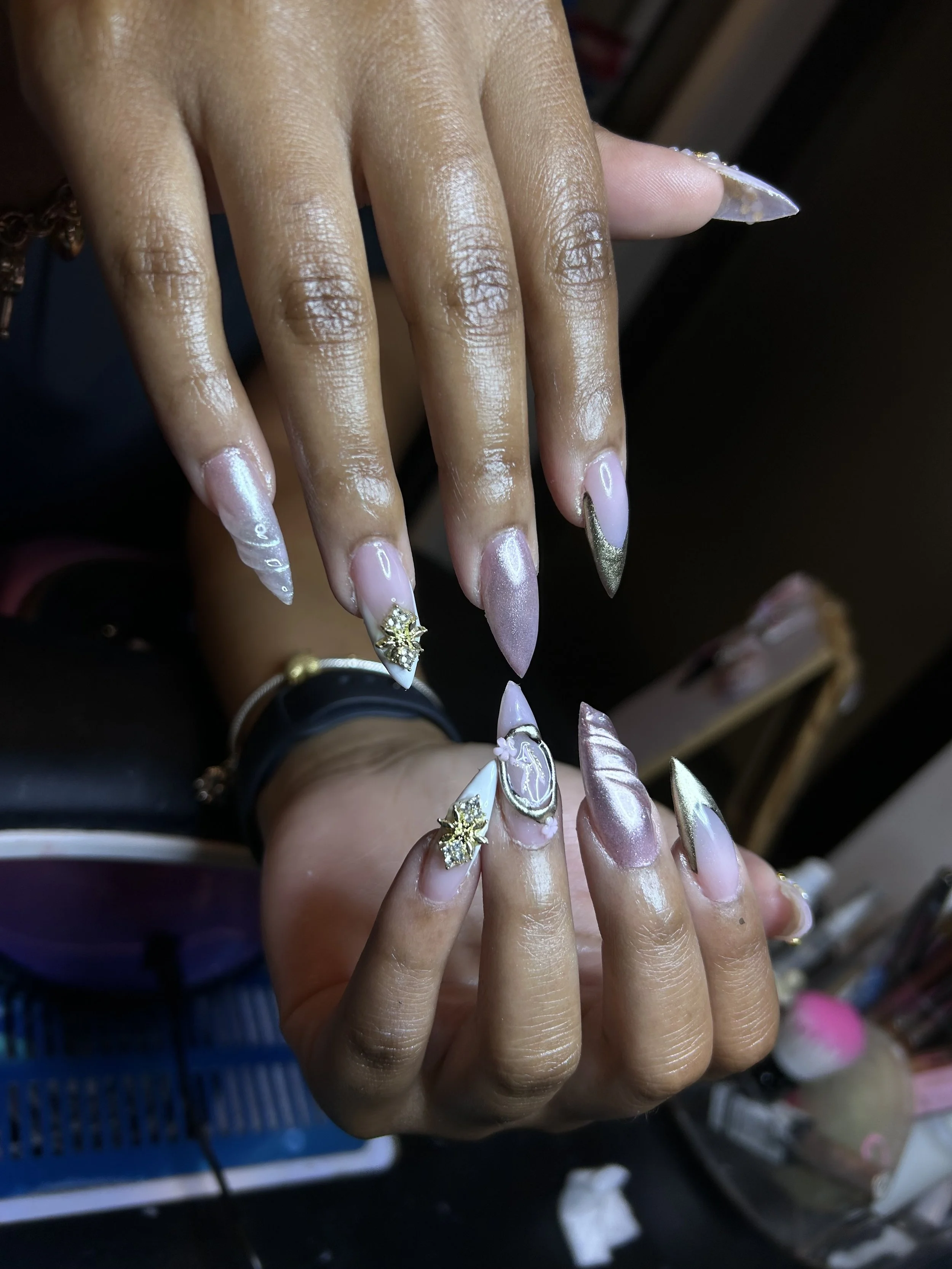 Close-up of a person's hands with elaborate gel nail art featuring pink, white, and gold colors, 3D decorations, and rhinestones.