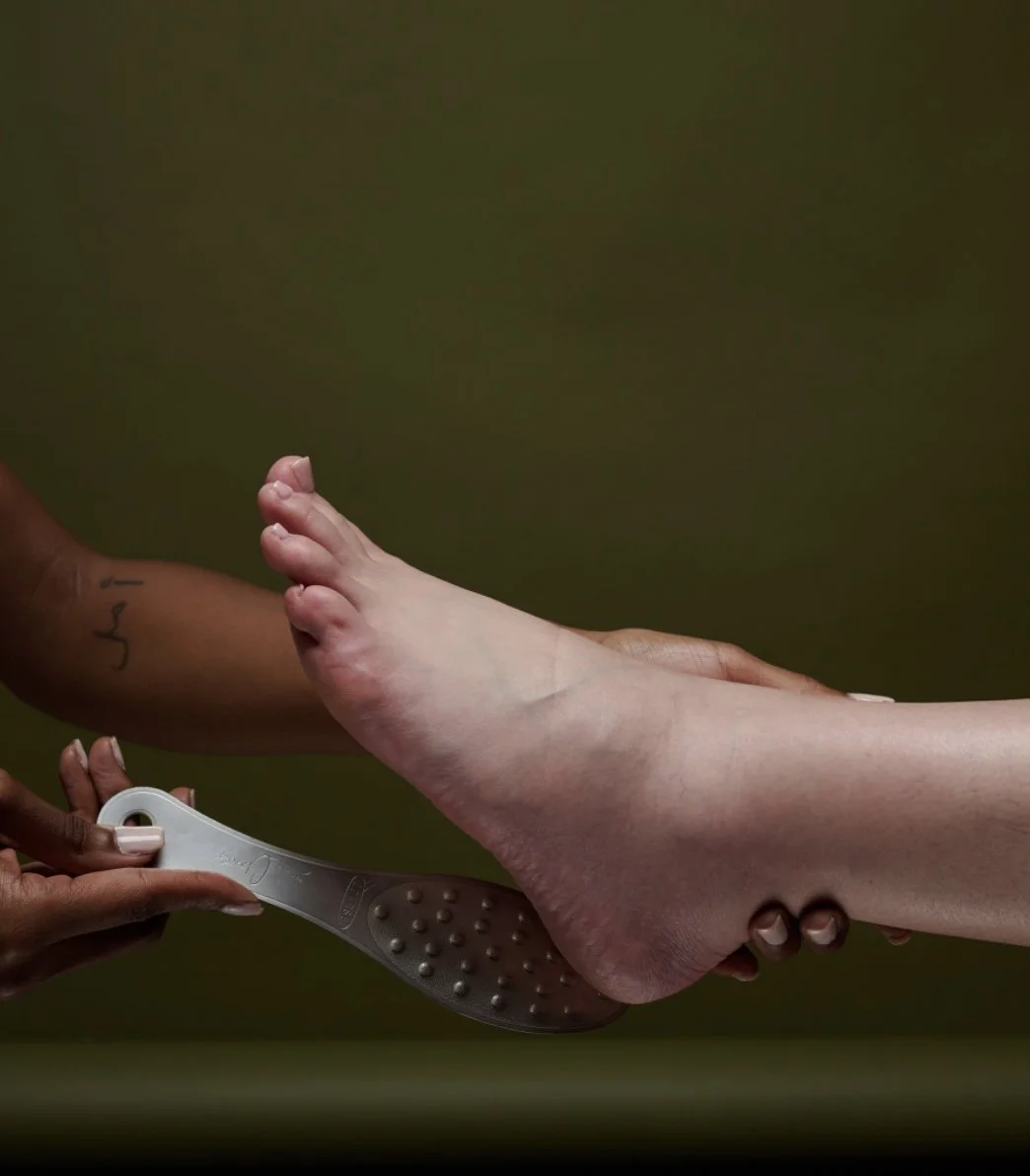 A person receiving a foot massage with a massage tool, focusing on the sole of the foot, against a plain background.