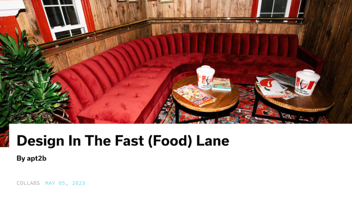 A cozy corner with a red velvet banquette, wooden walls, and two round coffee tables covered with KFC buckets, magazines, and a menu.