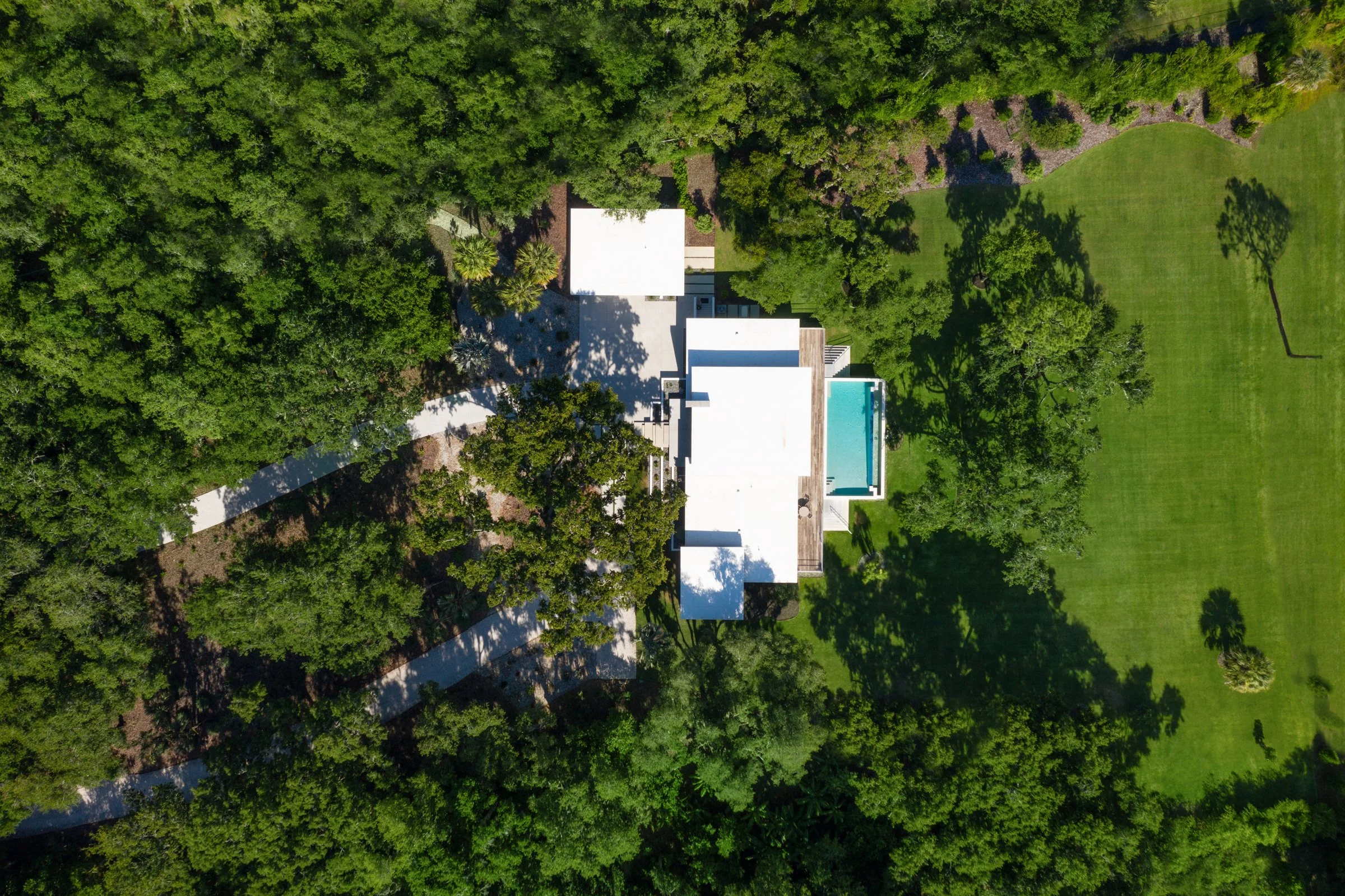 Aerial view of a modern house with a swimming pool, surrounded by trees and green lawn.