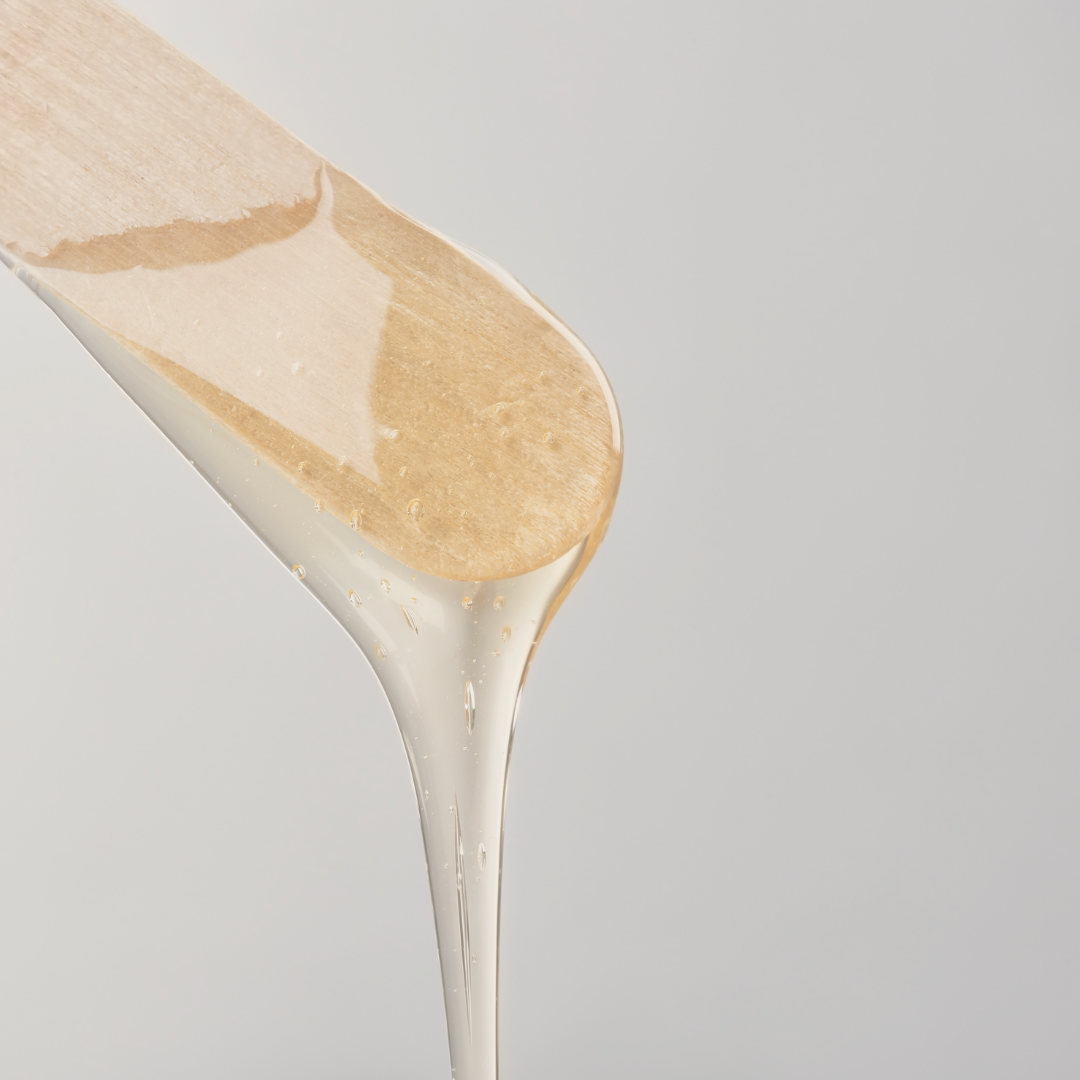 Une spatule en bois versant de la cire au miel sur une surface blanche pour les épilations.