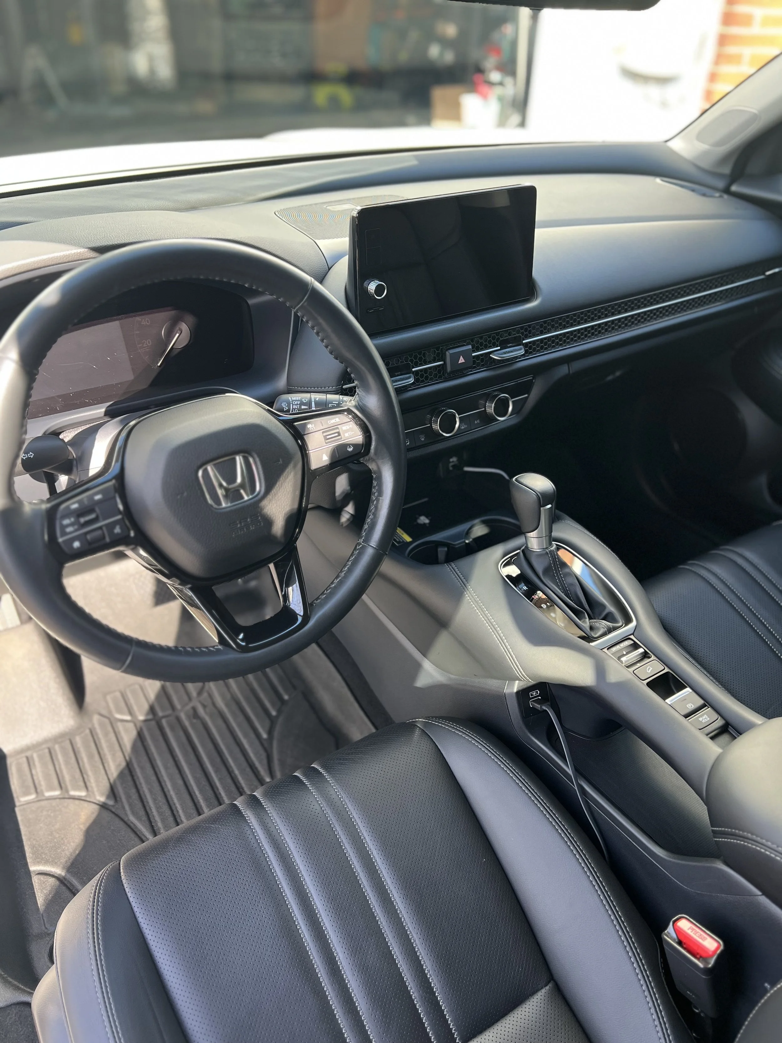 Interior view of a modern Honda car, showing the steering wheel, dashboard, center console with gearshift, and black leather seats.