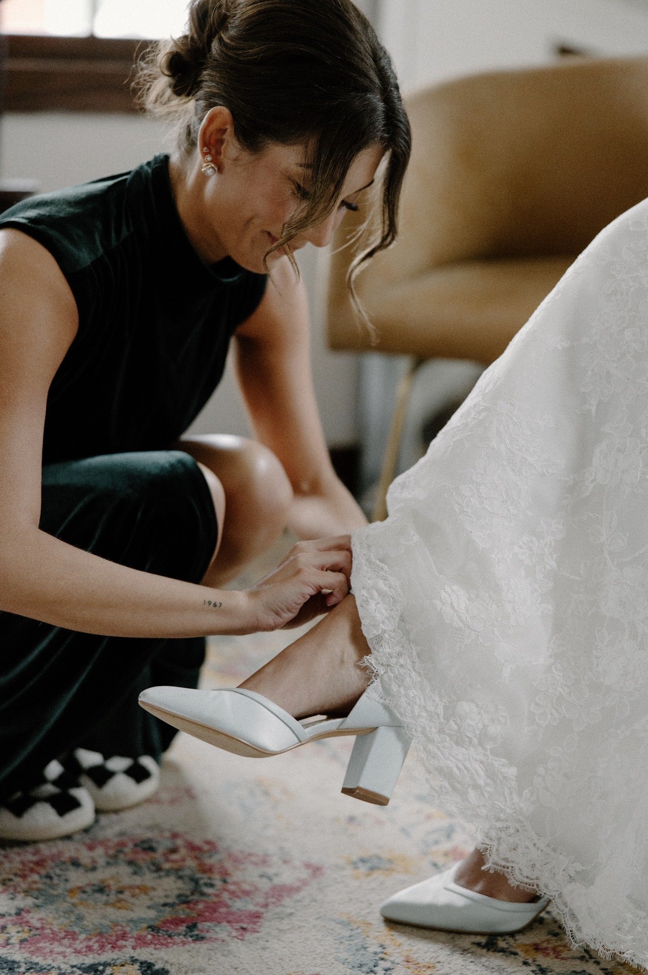 Delaney's friend bending down to help her put on her white heel..