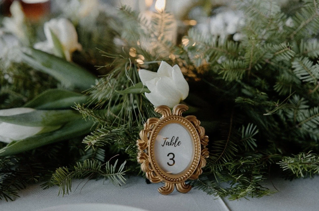 A table setting at a wedding. Says Table 3 in a small gold frame with green and white center piece behind it.