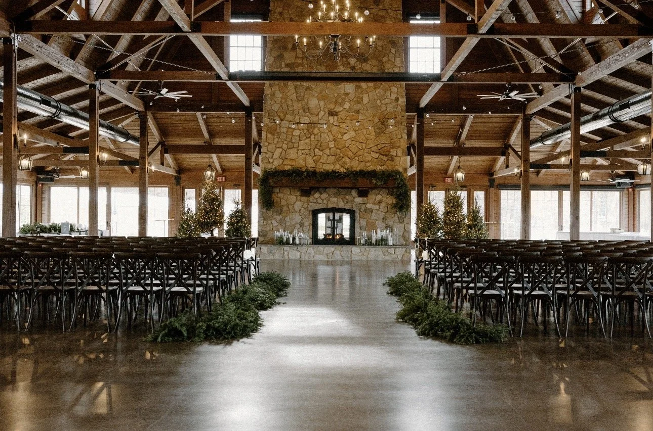 Delaney's wedding venue. Isle is lined with pine on the floor, dark wood chairs on both sides, very big stone fireplace going from the floor to the ceiling, wood beams going across the entire top of the building, etc.