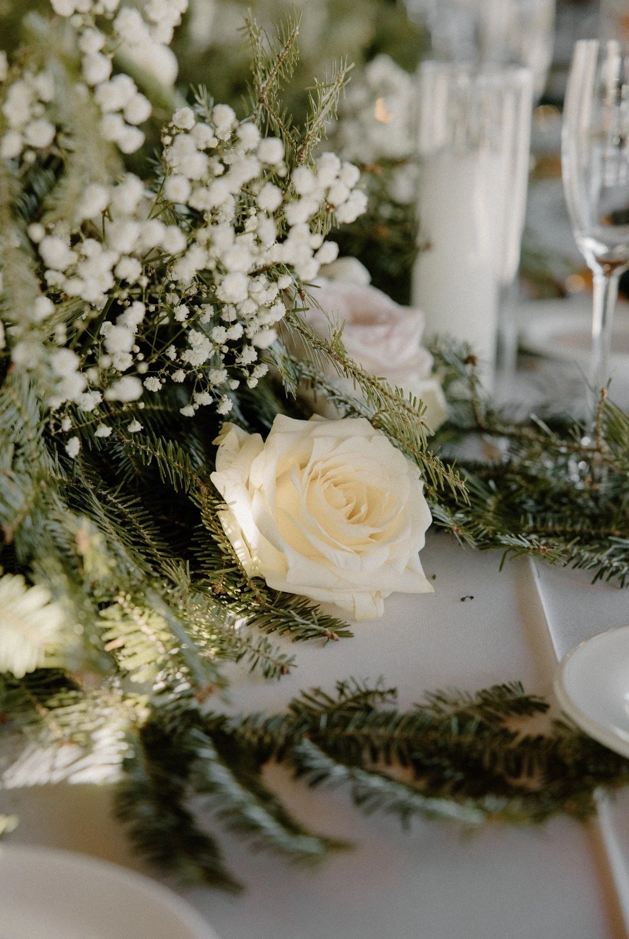 Delaney's white rose table decor with green pine and other small white flowers.