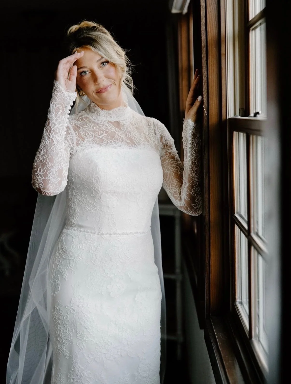 The founder and owner of the company posing for her photos on her wedding day. She is in a white lace gown, her hair is up, she is looking at the camera with a soft smile on her face.