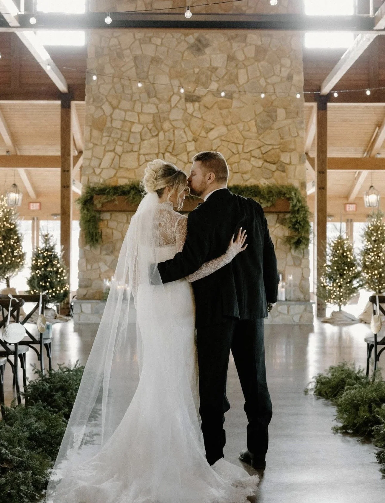Delaney and her husband standing in the middle of their venue, with him kissing her on her forehead and her leaning in and a soft smile.