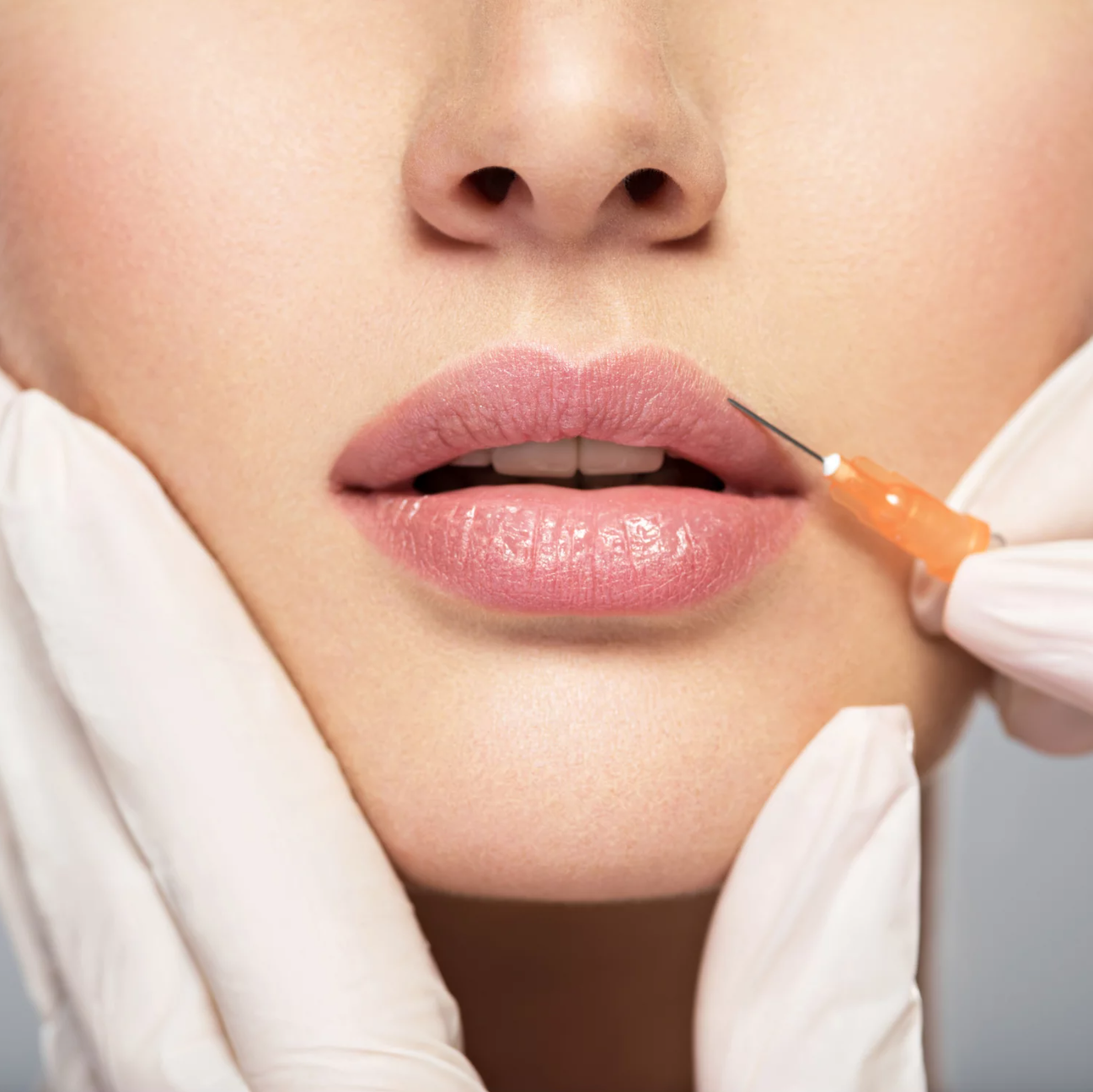 Close-up of a person receiving a lip injection, with a medical professional wearing gloves administering the shot near the person's lips.