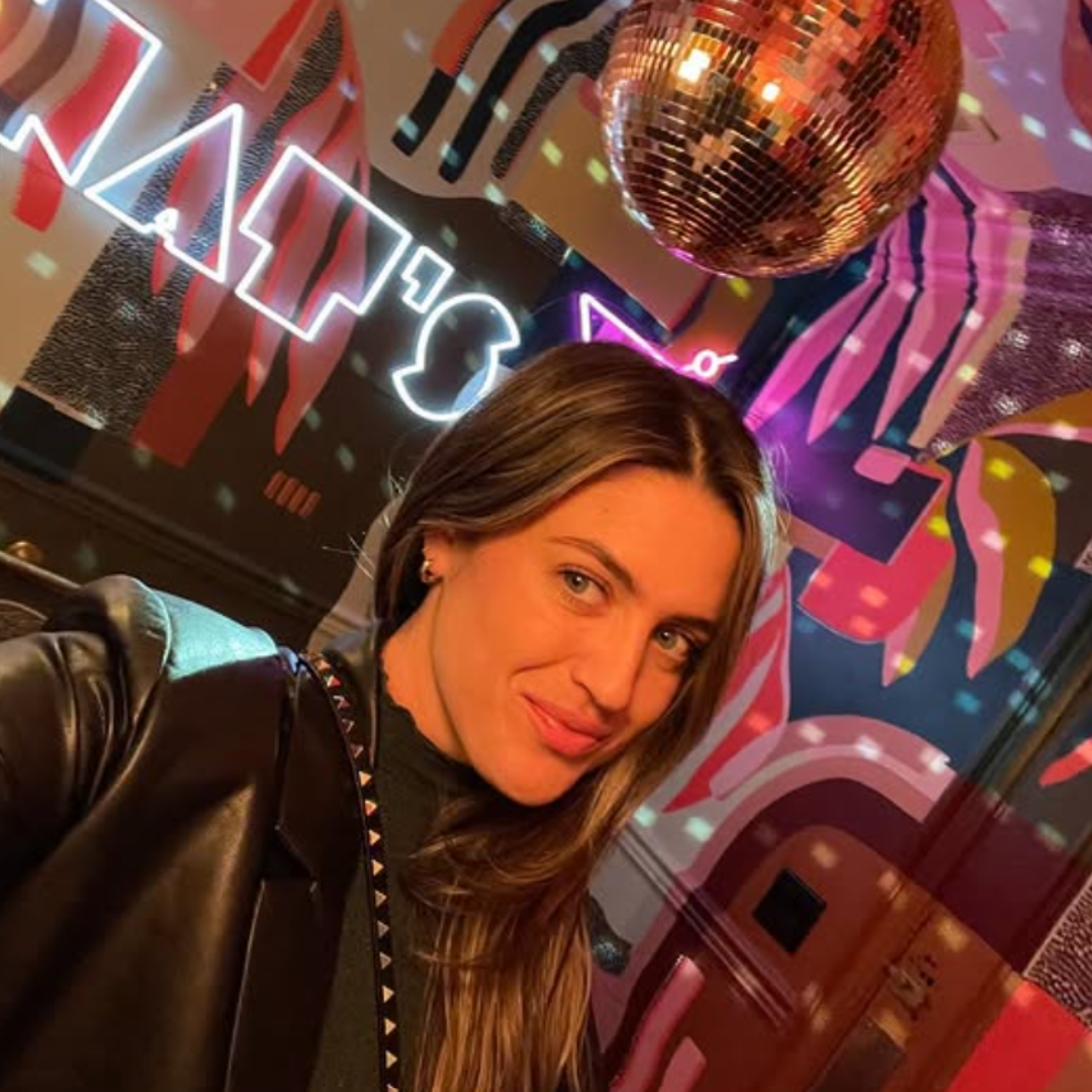 A woman taking a selfie in a colorful, neon-lit room decorated for a party with a disco ball hanging from the ceiling.