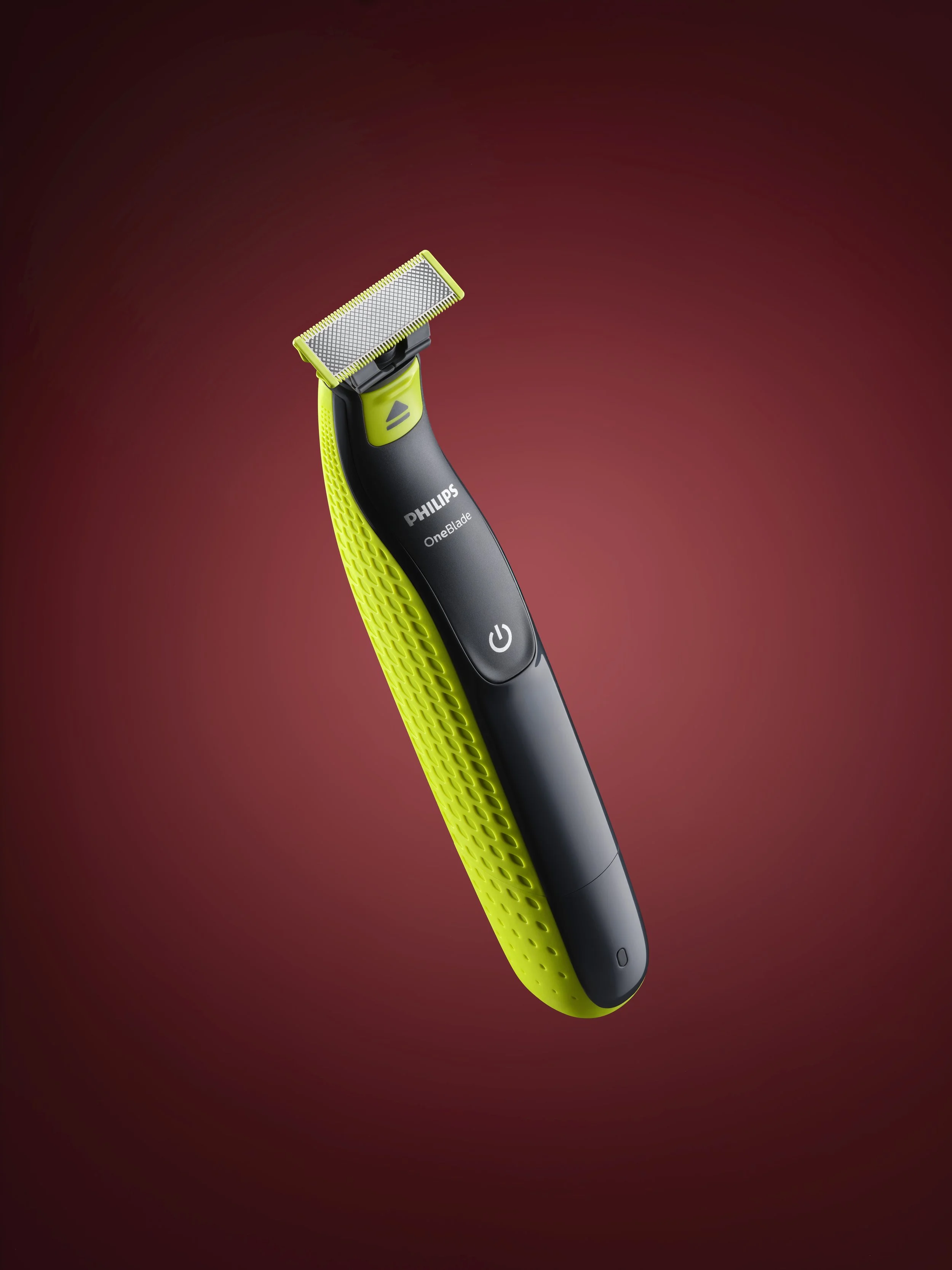 rasoio elettrico Philips OneBlade con manico nero e dettagli verde lime, su sfondo rosso scuro.