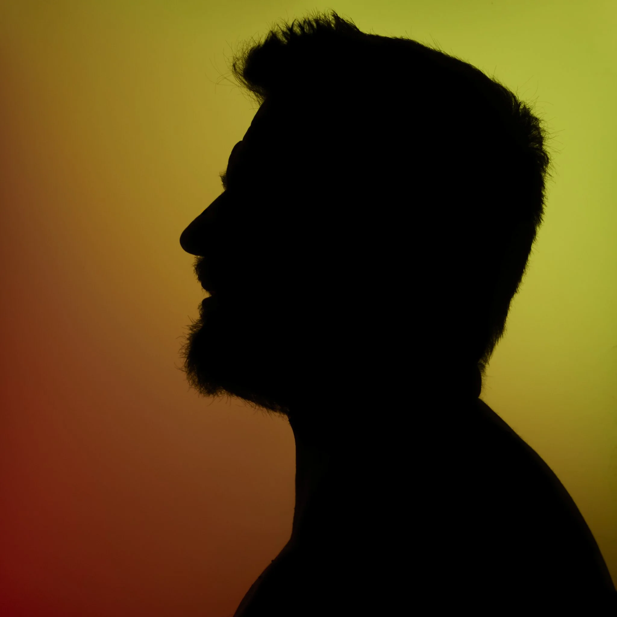 Silhouette di un uomo con barba sui toni caldi dell'arancione e del giallo.