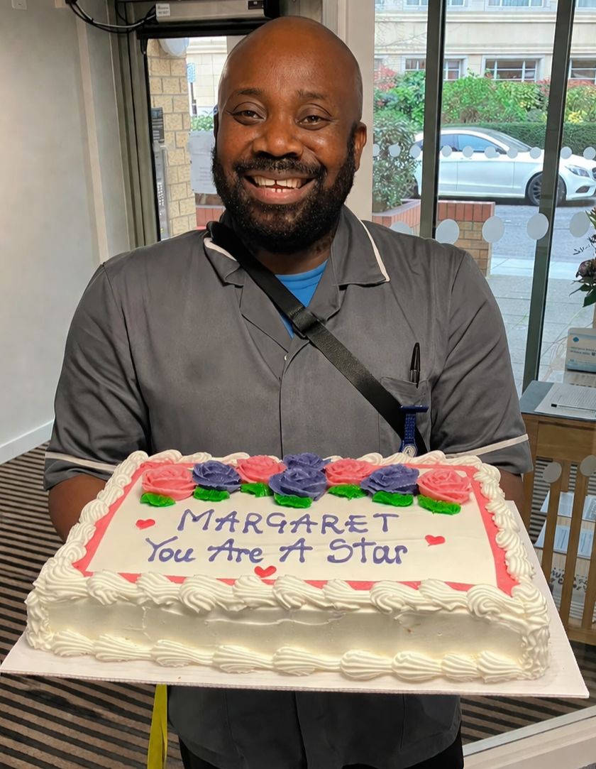 A carer is smiling with joy as he holds a cake to celebrate a resident after a successful day of easy and fun filming for a Legacy Film commissioned by an individual who lives in his care home