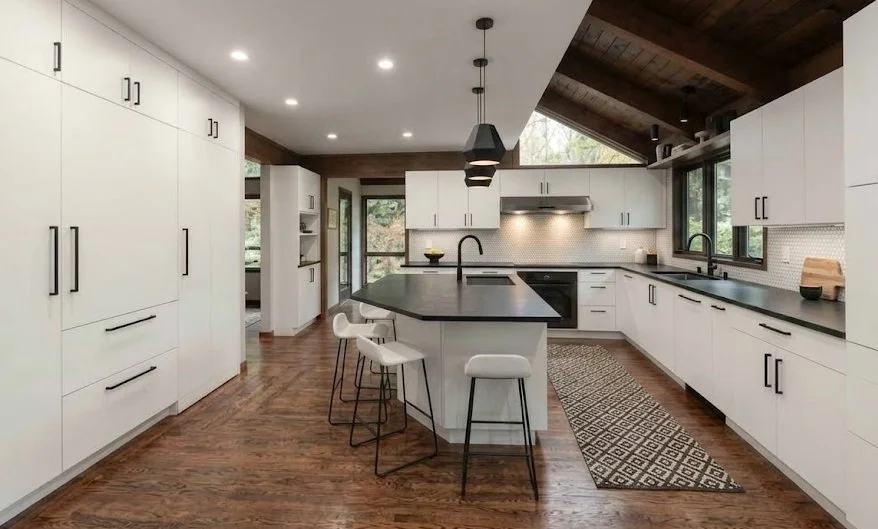Kitchen remodel showcasing the trend of flat-panel cabinet doors, featuring sleek, easy-to-clean white slab cabinetry, contrasting dark countertops, a central island, and warm wood accents