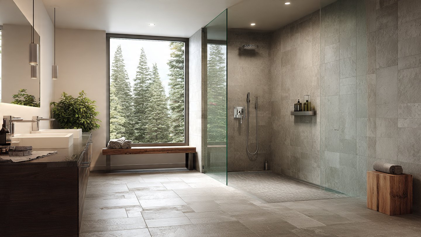 A modern Northern Michigan bathroom remodel featuring a zero-threshold curbless shower. Continuous grey floor tile flows seamlessly into the glass-enclosed shower, complemented by a double vanity and a large window overlooking evergreen trees.