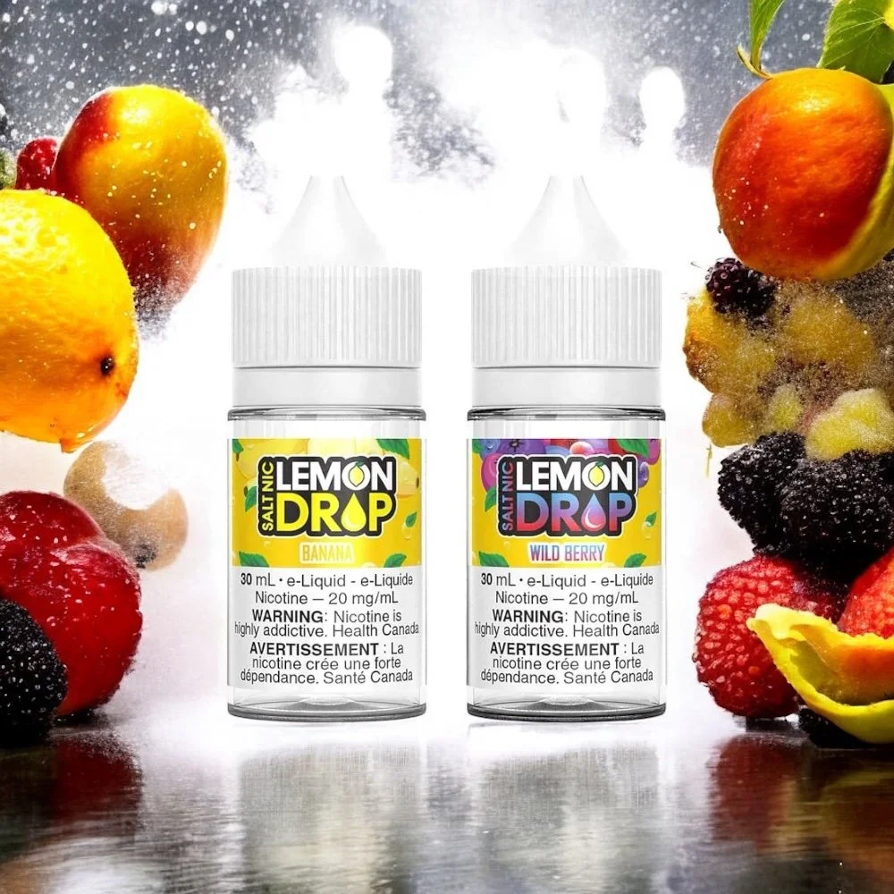 Two bottles of Lemon Drop e-liquid flavor, Banana and Wild Berry, surrounded by fresh fruits including apples, strawberries, blackberries, and lemon, with a sparkling background.