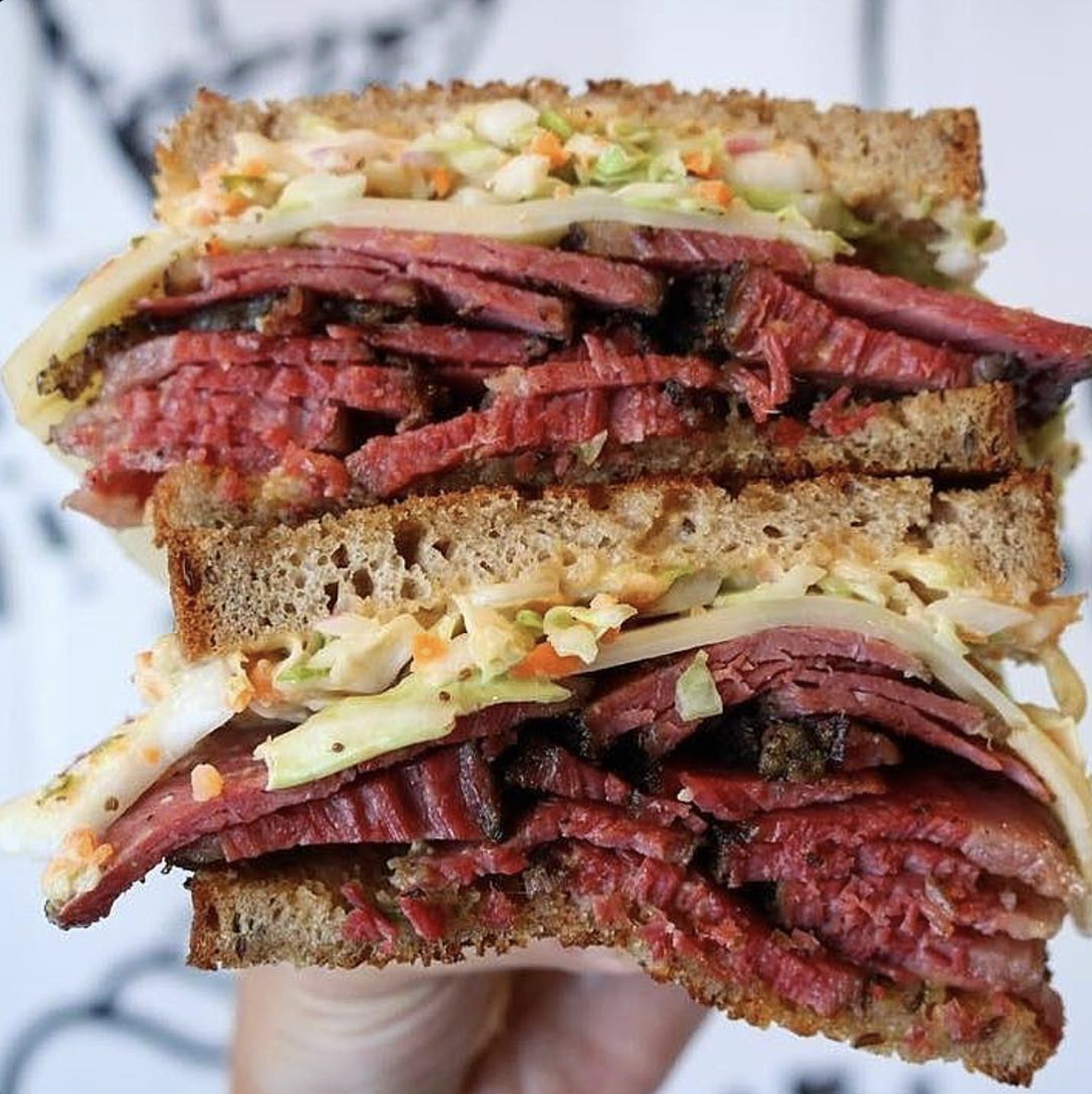 a stacked pastrami sandwich with rye bread, swiss cheese and coleslaw takes up full image