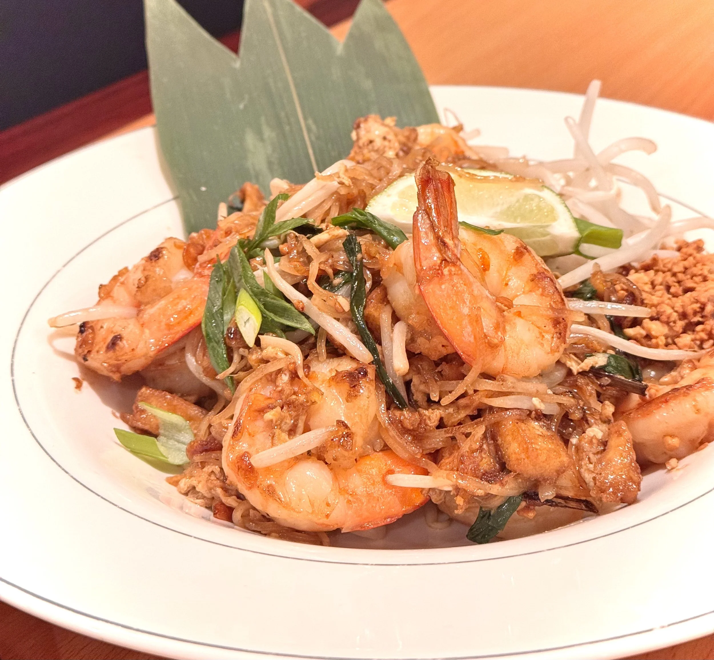 A plate of pad thai with shrimp, bean sprouts, green onions, lime wedge, and chopped peanuts.
