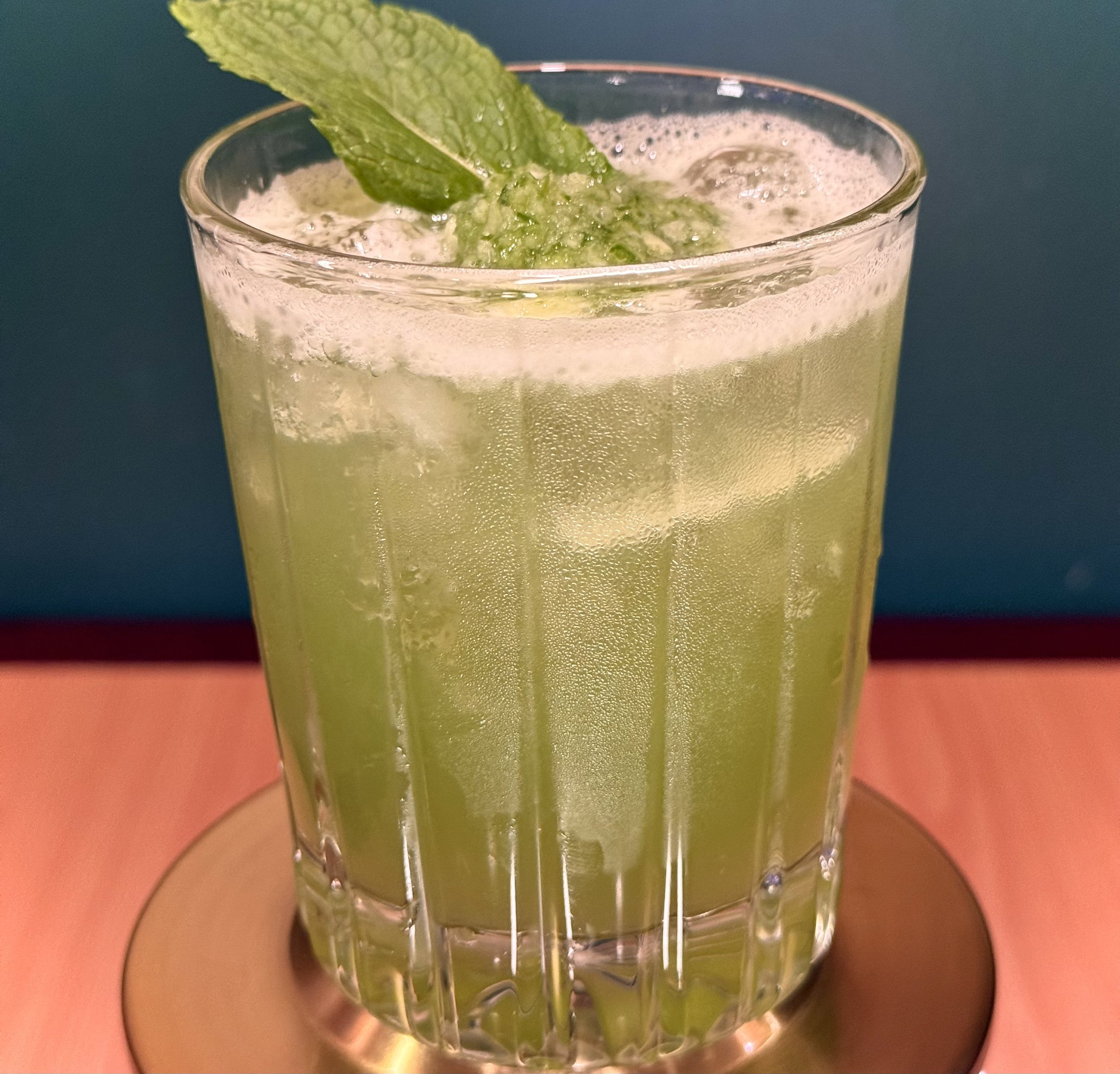 A glass of green cocktail garnished with a fresh mint sprig