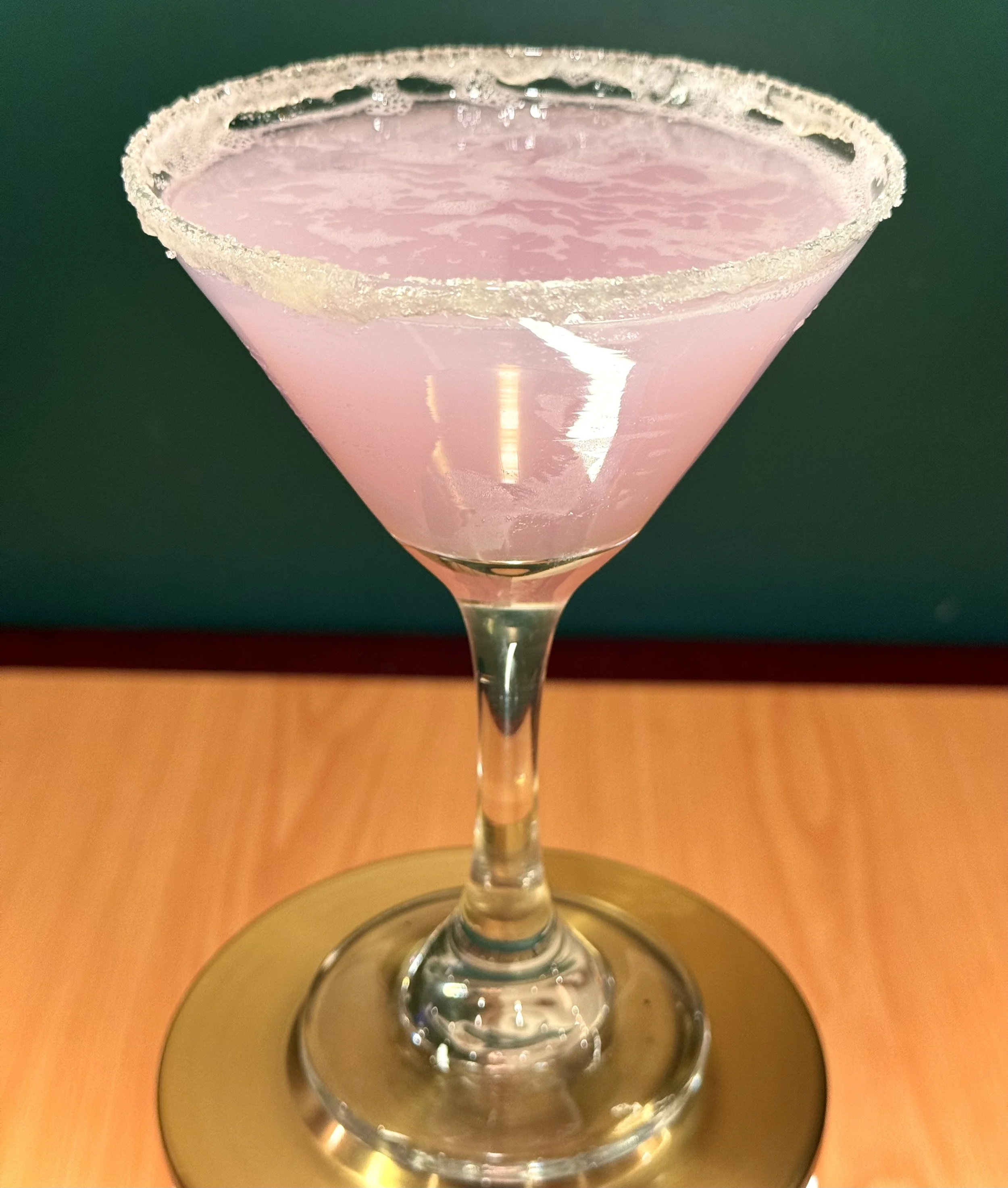 Pink cocktail with a salted rim in a martini glass on a wooden surface.