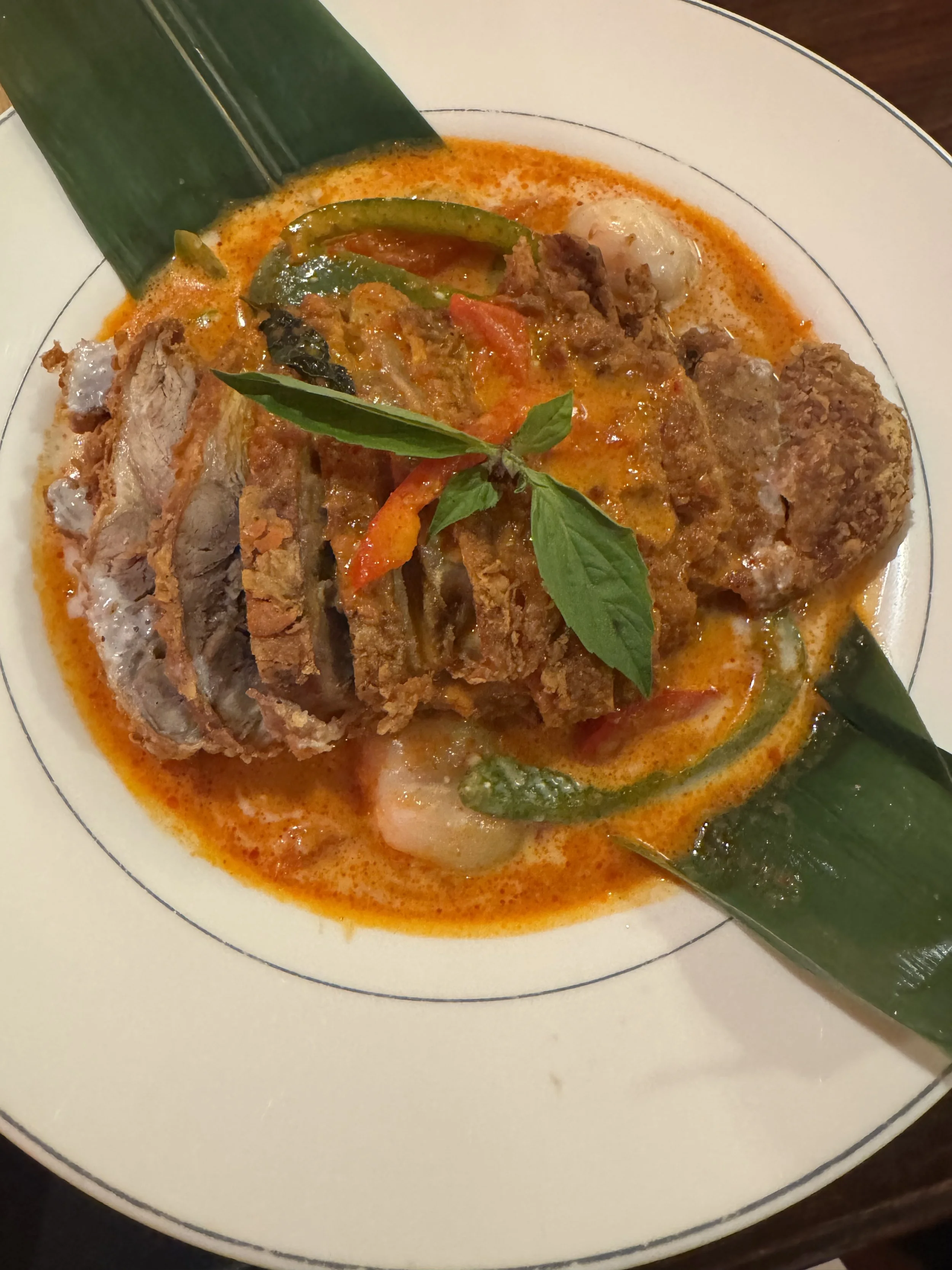 Plate of Thai green curry with rice, basil leaves on top, and pieces of meat and vegetables in a spicy coconut sauce.