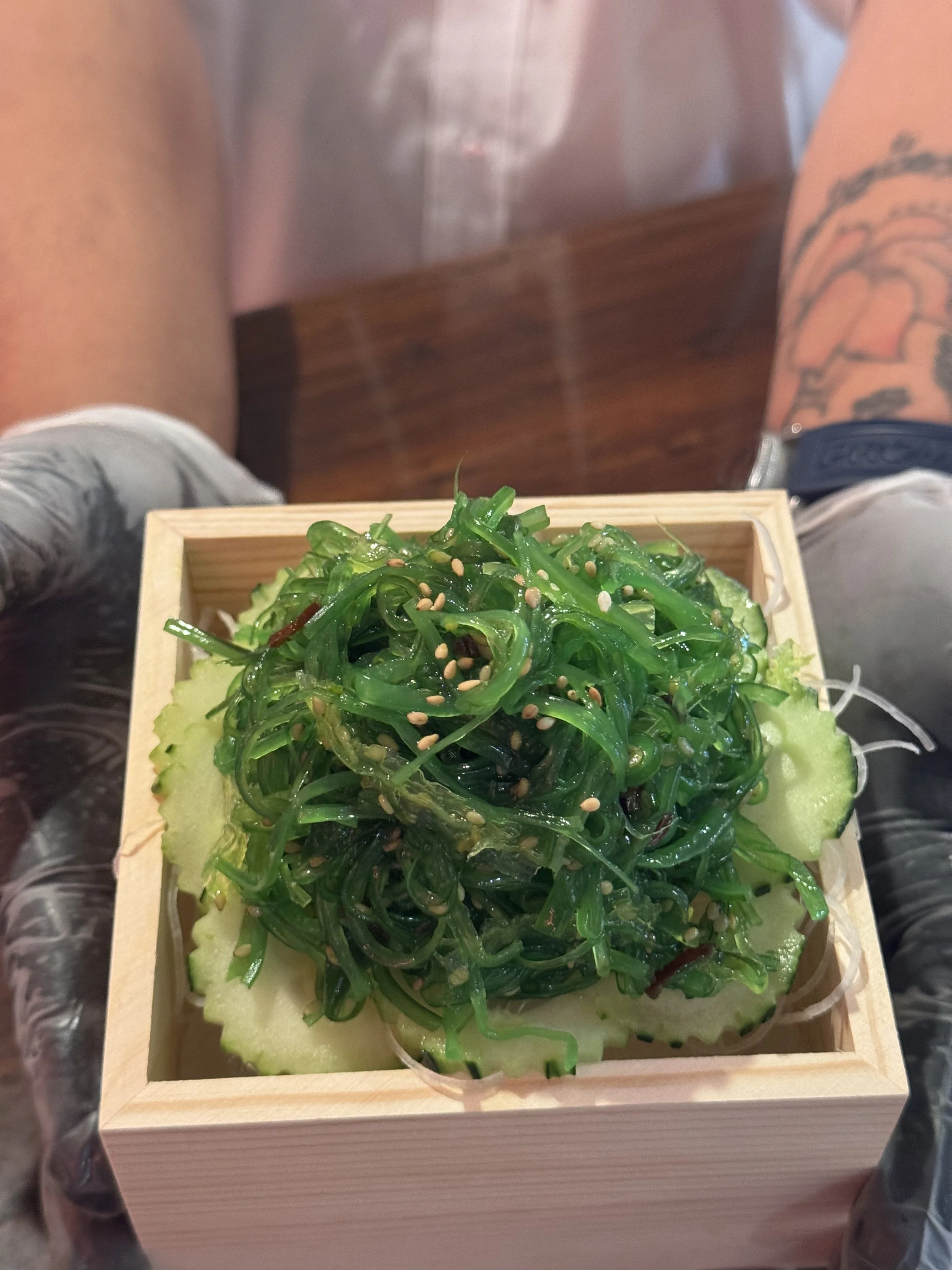 Seaweed salad with sesame seeds, served on cucumber slices in a wooden box.