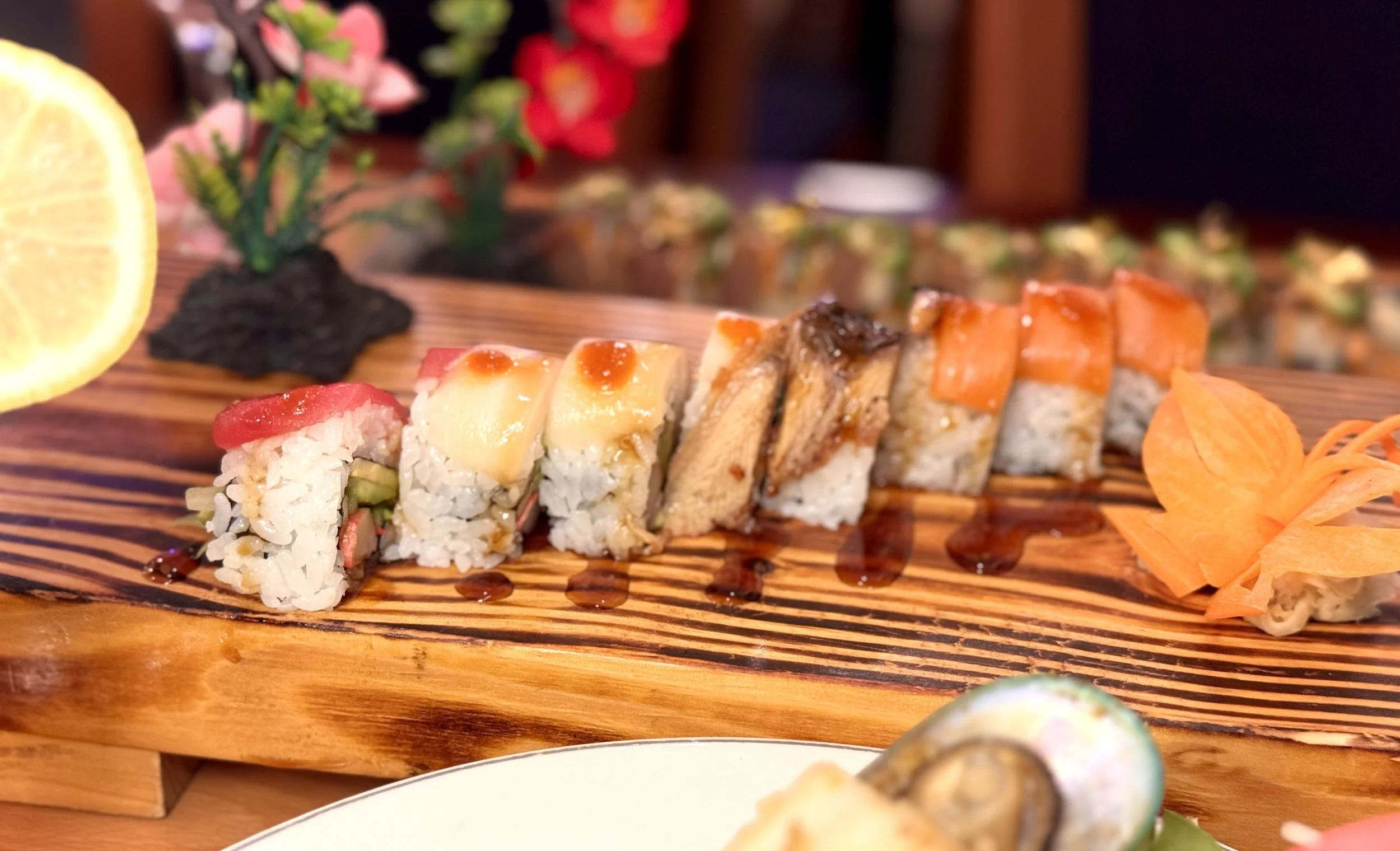 Assorted sushi rolls on a wooden platter with lemon wedge, pickled ginger, and soy sauce drizzle.