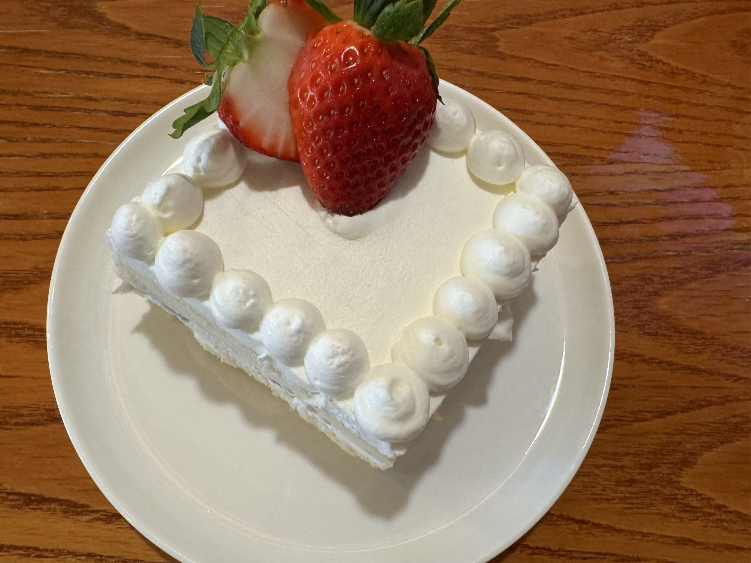 Square slice of white cake with white frosting border topped with three strawberries, two halved and one whole, on a white plate.