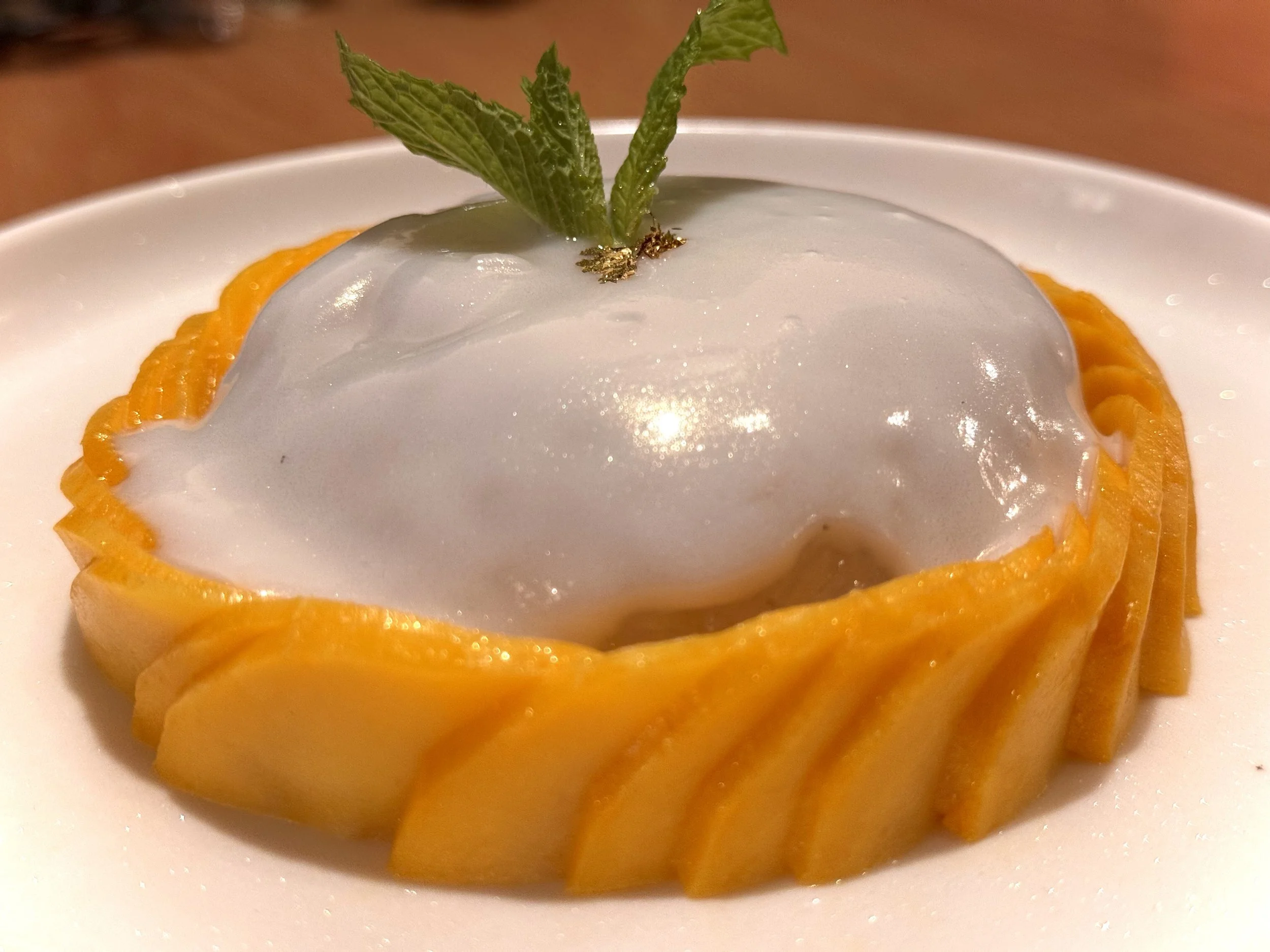 Fresh mango slices arranged around a white dessert topped with a mint leaf.