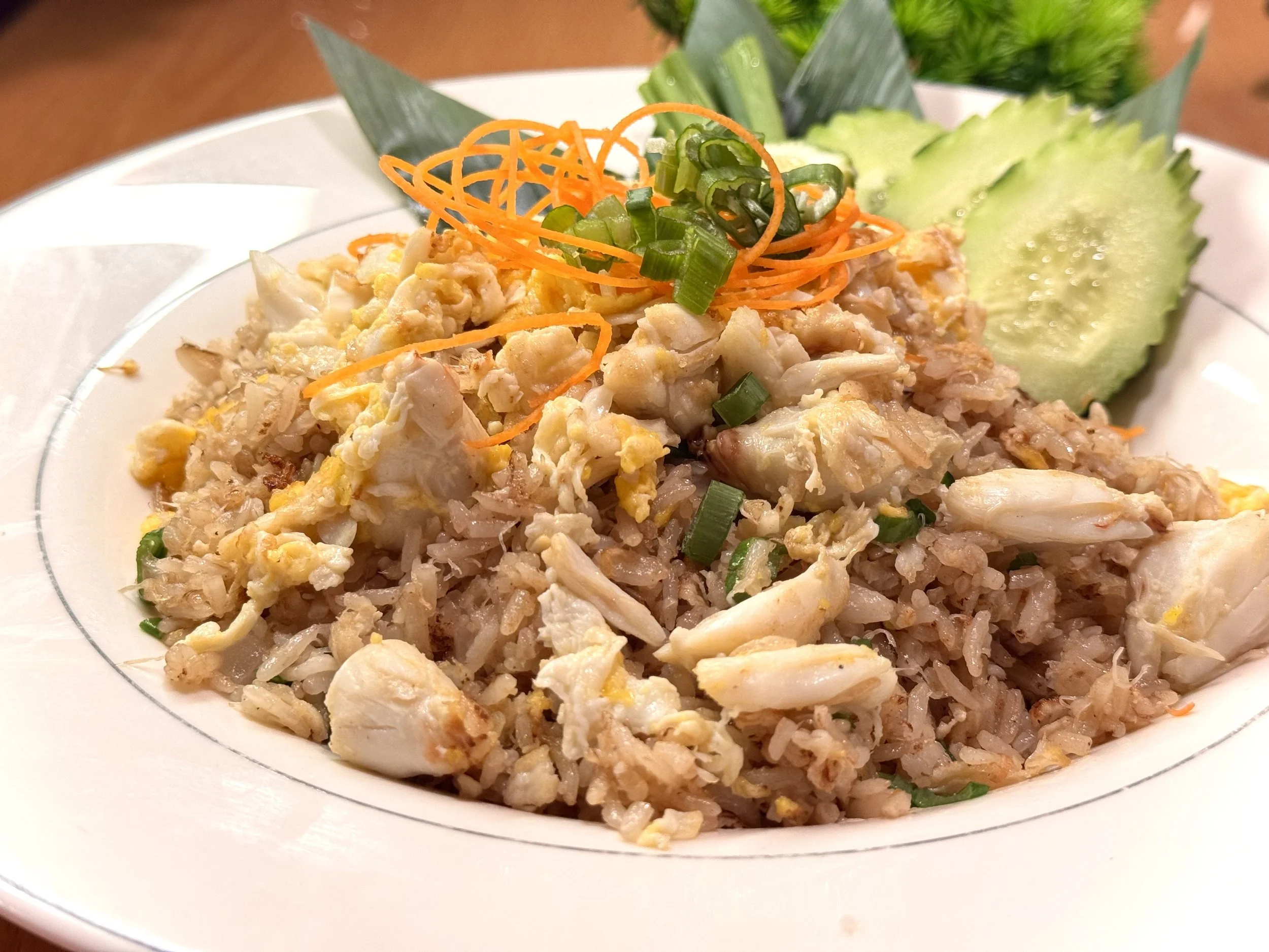Plate of fried rice with chopped chicken, scrambled eggs, and chopped green onions, garnished with shredded carrots, sliced cucumber, and a piece of pineapple.