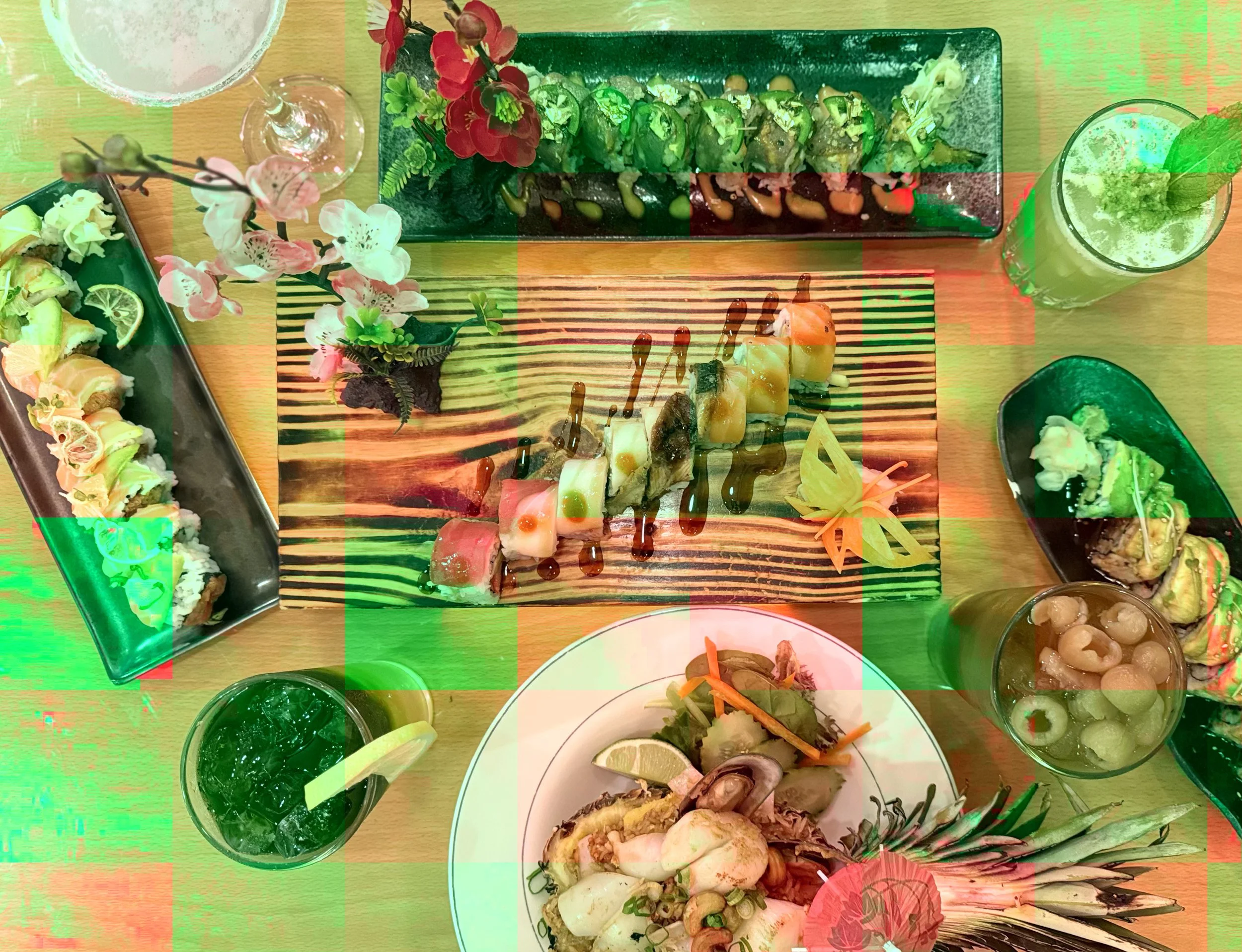 Top-down view of a table with various sushi dishes, drinks, and garnishes, including sushi rolls, sashimi, and beverages with lime slices and mint.