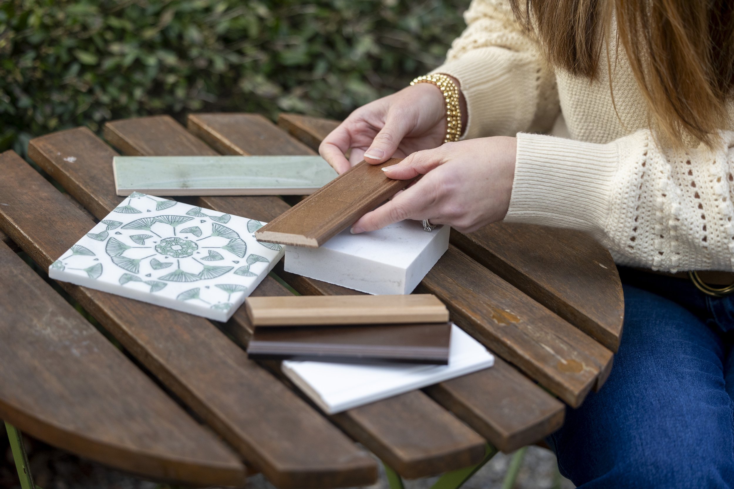 Person in beige sweater sitting at a wooden table, selecting color or material samples.