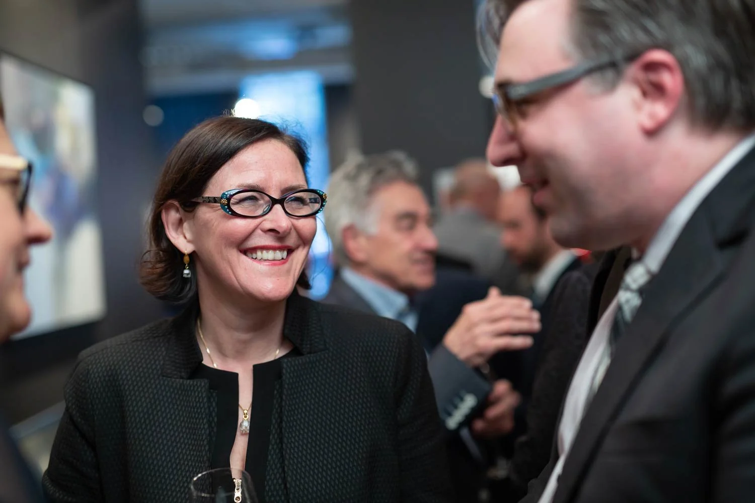 Une femme souriante avec des lunettes en conversation avec un homme dans un contexte professionnel.
