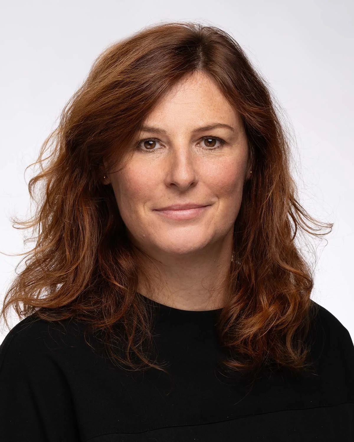 Photo d'une femme avec des cheveux roux, souriant, portant un haut noir, fond blanc.