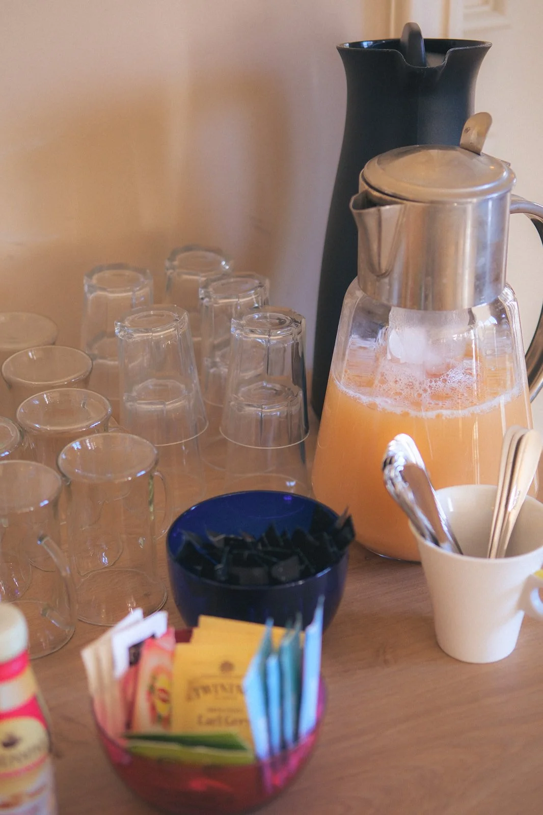 Une table avec une carafe de jus d'orange, plusieurs verres, une théière noire, une tasse avec des cuillères, un bol avec des sachets de thé, et des petits contenants. Il s'agit des boissons d'accueil du séminaire stratégique.
