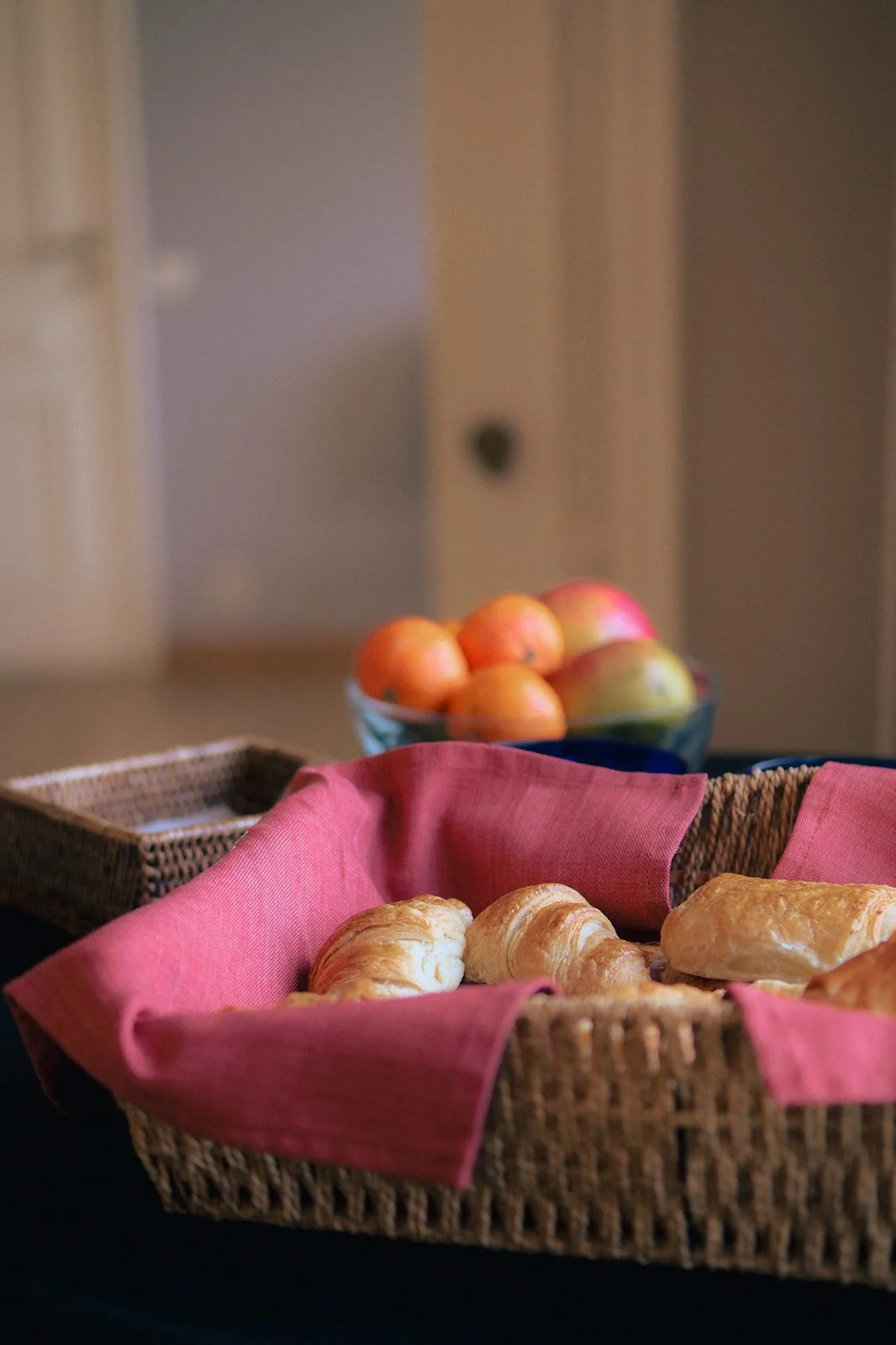 Un panier en osier avec des croissants. En arrière-plan, fruits proposés pour l'accueil café des participants à la réunion à Walhain.