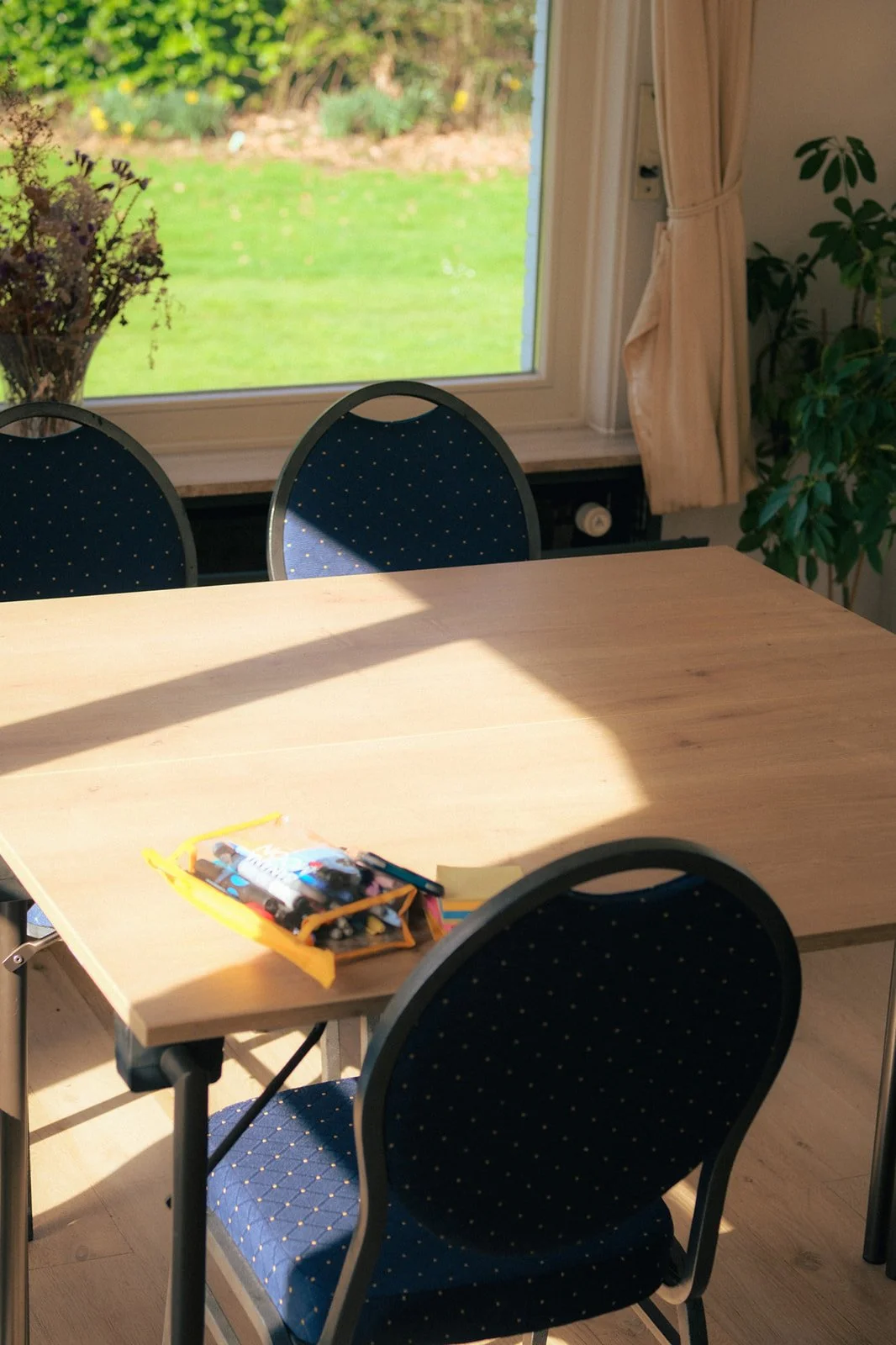 Une table en bois clair avec des chaises bleues à pois blancs, dans une salle de réunion premium près d'une fenêtre laissant passer la lumière avec vue sur un jardin verdoyant. 