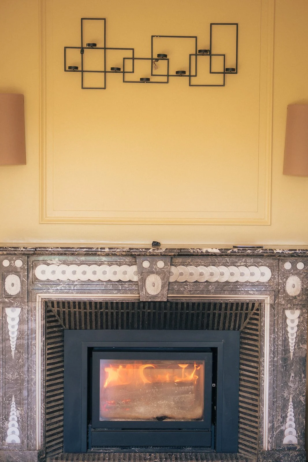 Cheminée en marbre avec un feu allumé, un mur jaune au-dessus avec une étagère noire de design moderne.