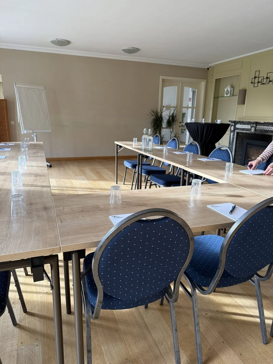Salle de réunion avec tables en bois, chaises bleues à pois, bouteilles d'eau et blocs-notes, en préparation pour une réunion.