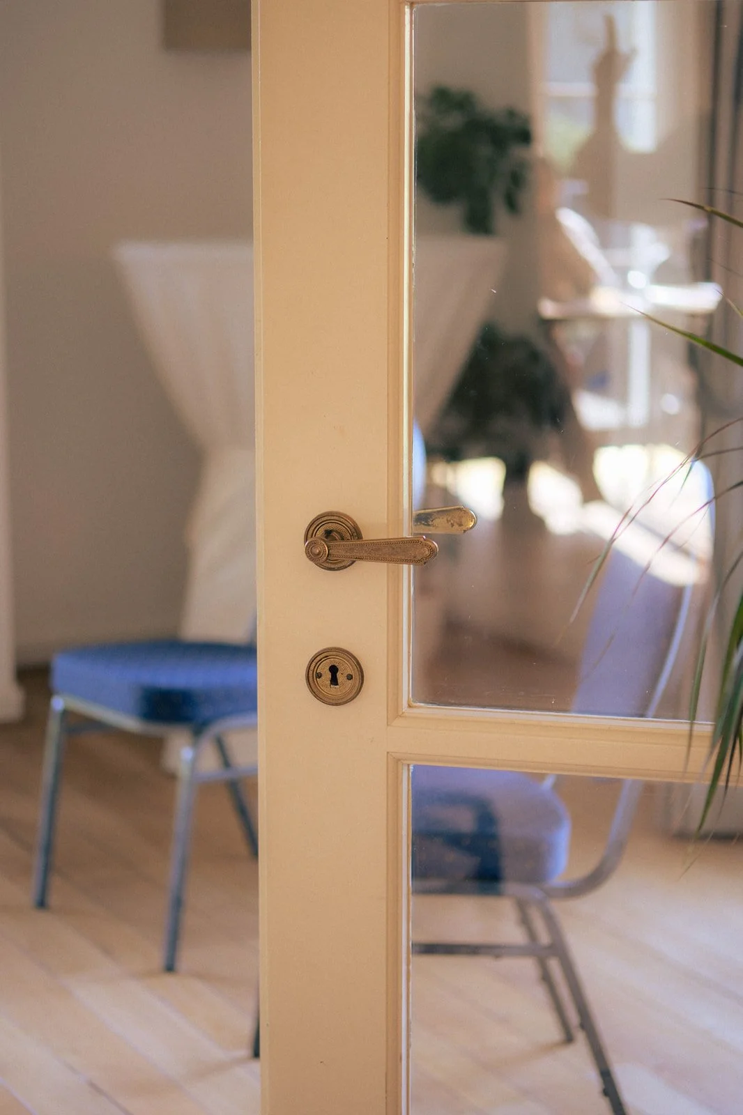 Vue partielle d'une porte en bois avec vitre, en arrière-plan une pièce avec un fauteuil bleu.