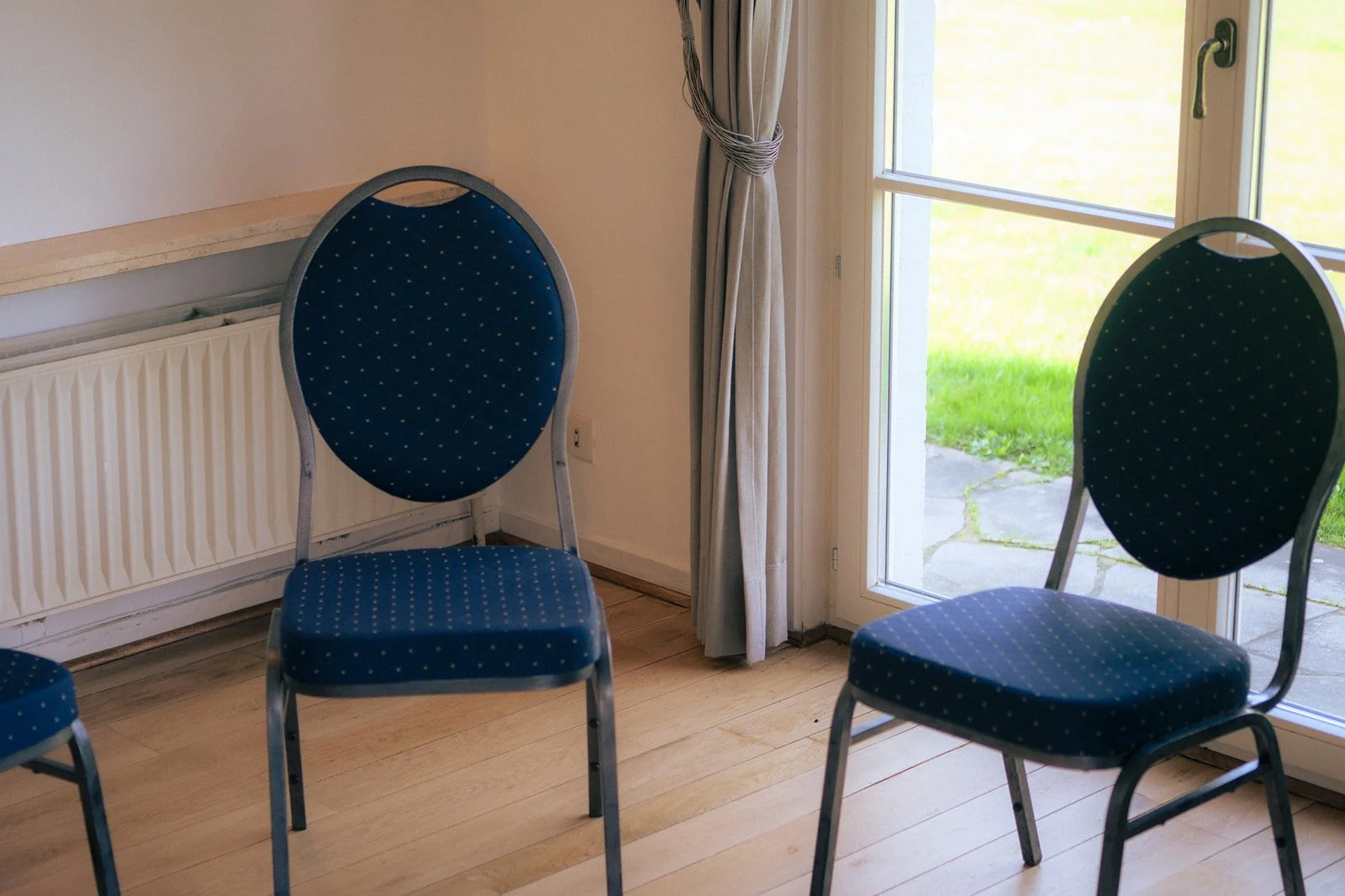 Quatre chaises avec une assise et un dossier en tissu bleu avec de petits points blancs dans une pièce près d'une porte-fenêtre donnant sur une terrasse en pierre et un jardin vert.