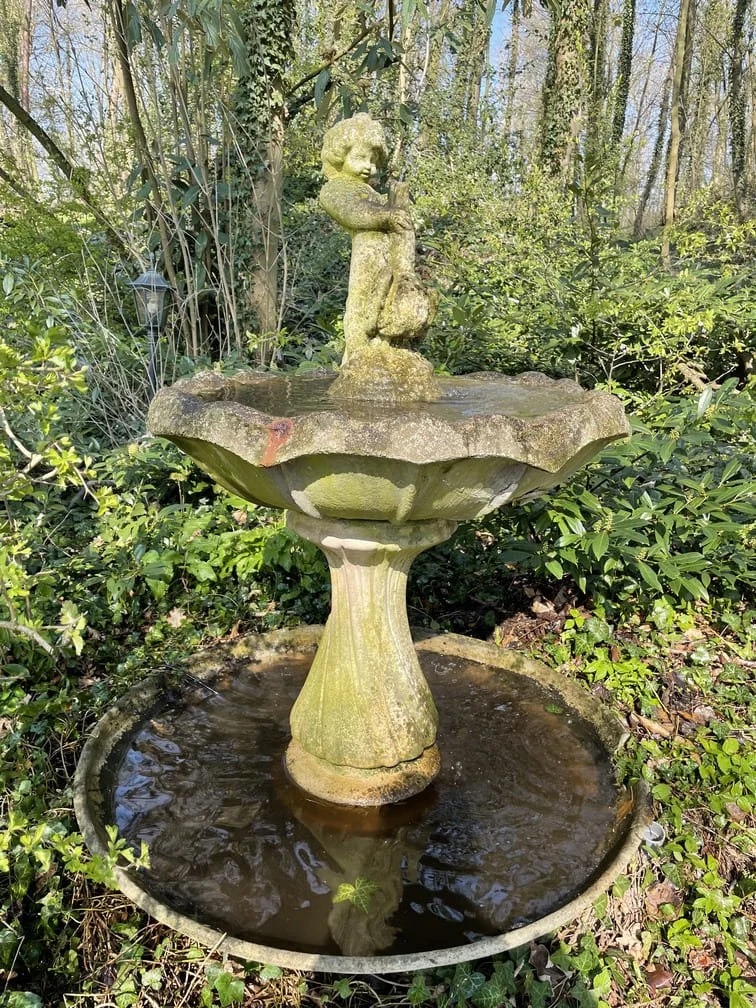 Une fontaine en pierre, entourée de végétation dans un jardin.