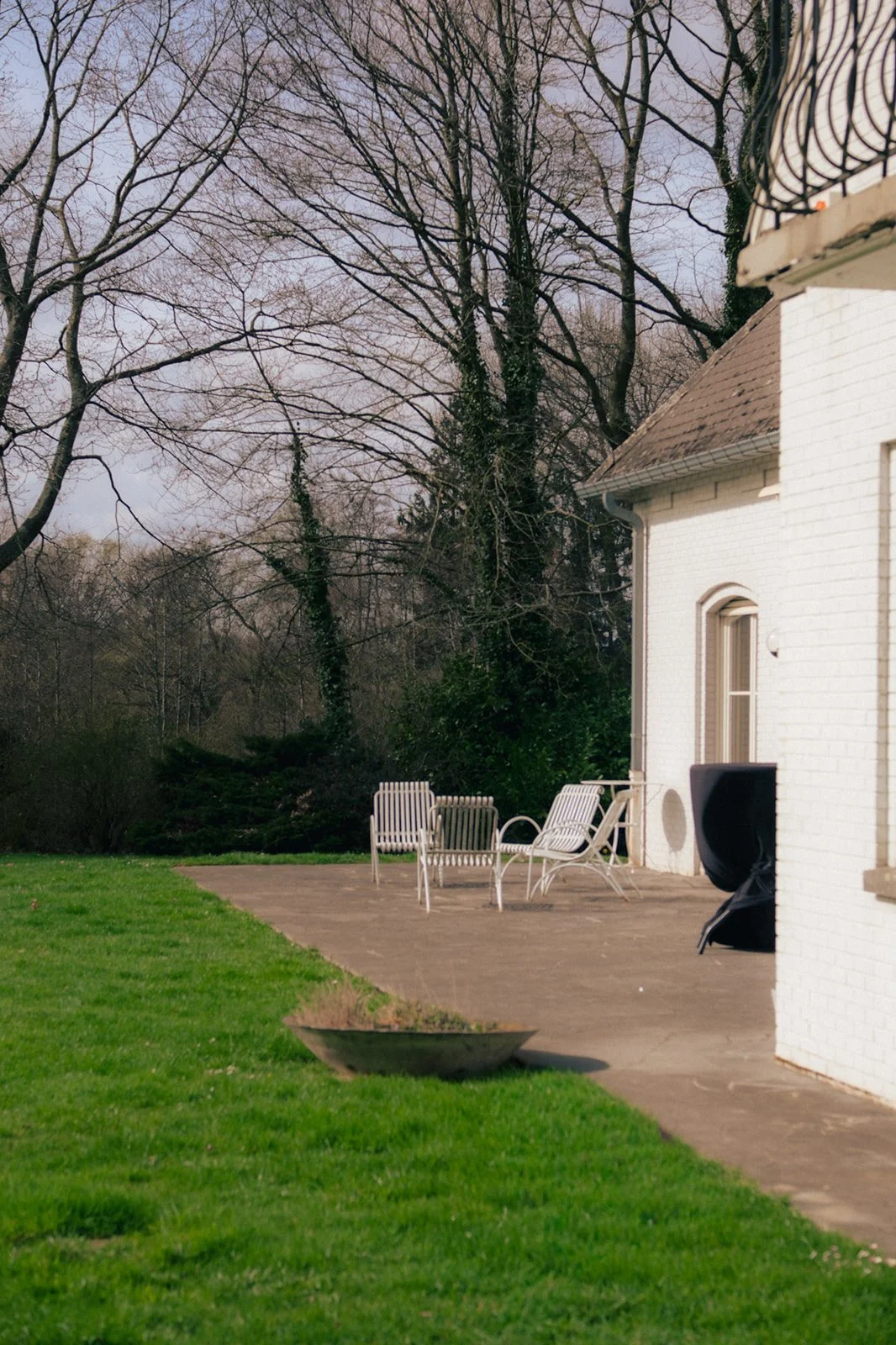 	La terrasse en pierre bleu devant la villa premium avec un mobilier de jardin composé de quatre chaises en métal blanc. La terrasse se trouve devant les salles de réunion. En arrière-plan, il y a des arbres.