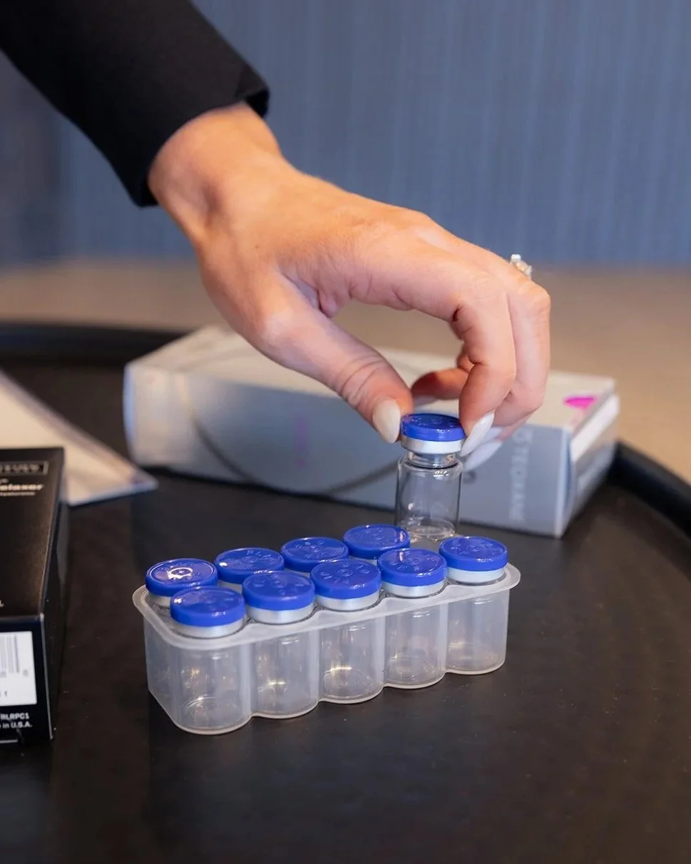A hand placing a small glass vial with a blue cap into a plastic holder with other vials.